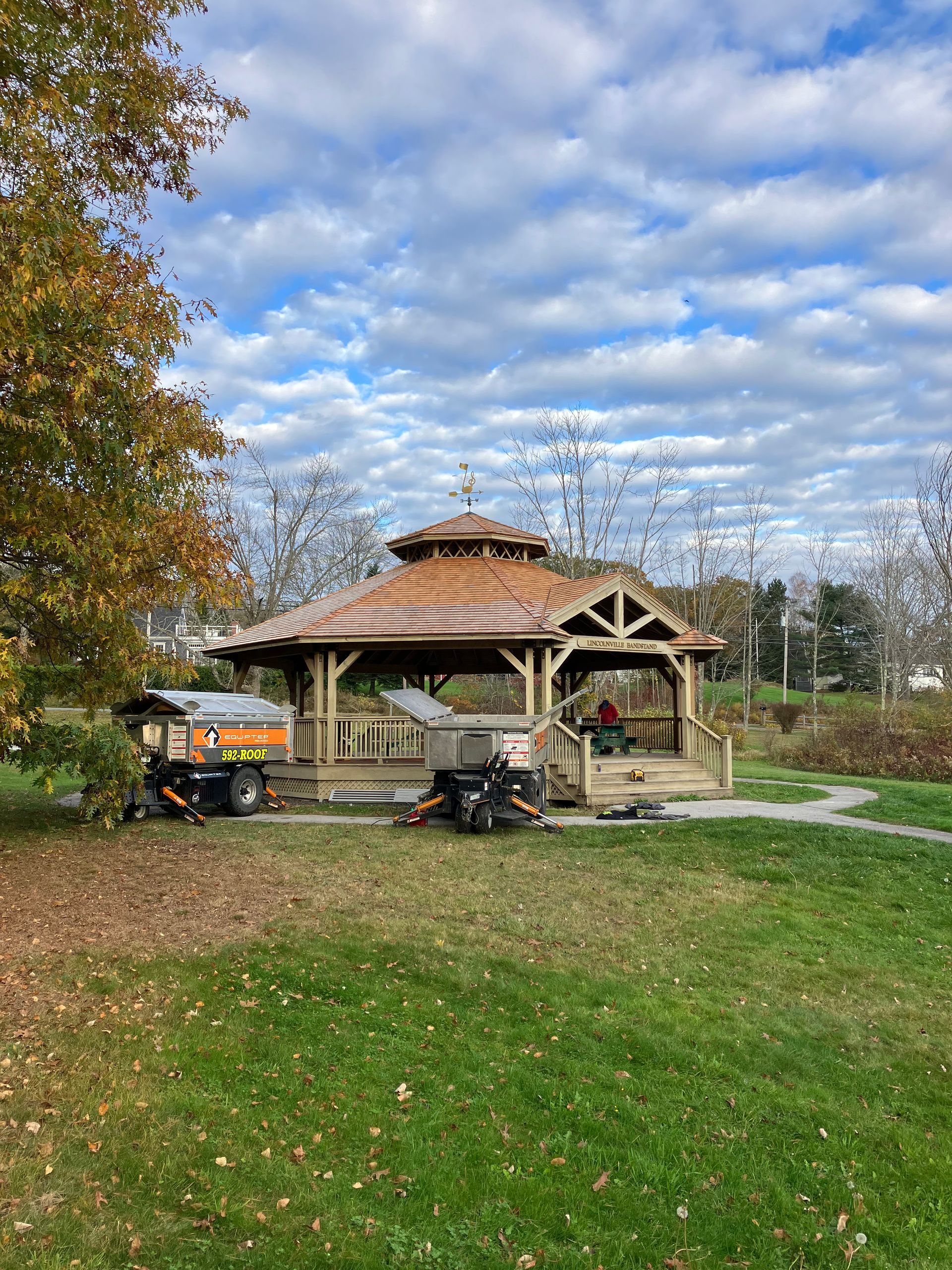 A gazebo in a park with a lawn mower parked in front of it.