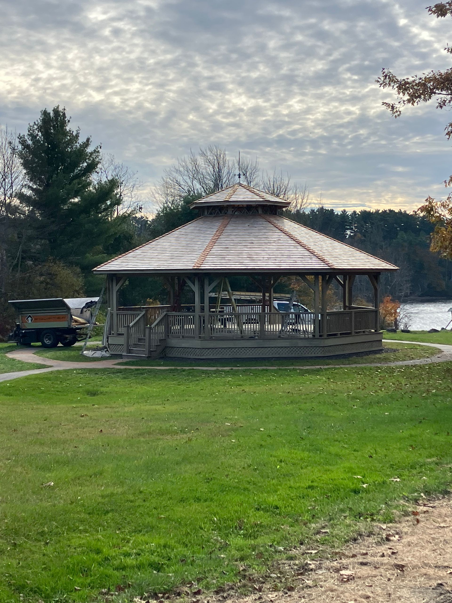 A gazebo is sitting in the middle of a grassy field next to a body of water.