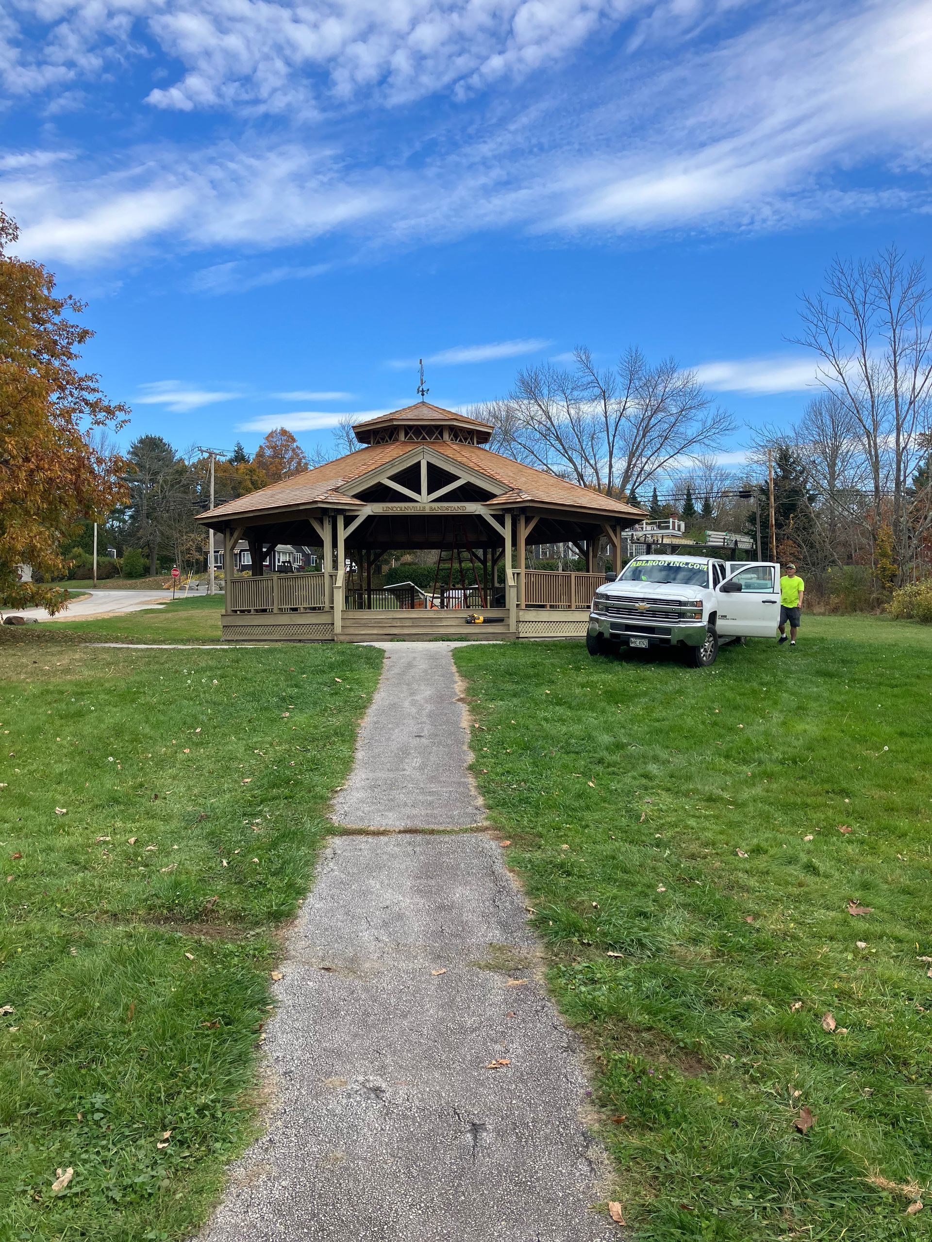 A white truck is parked in front of a gazebo in a park.