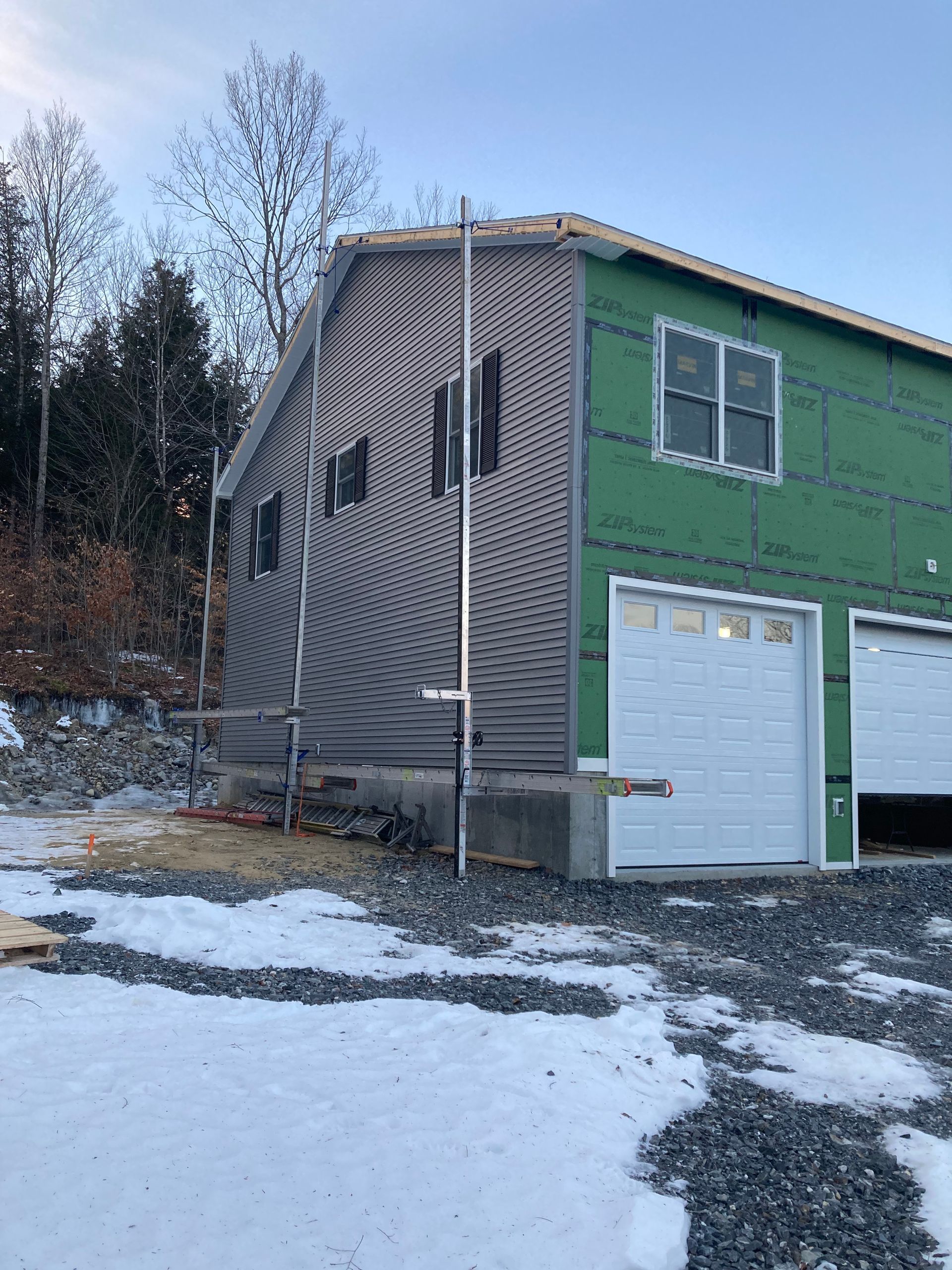 A house is being built with green siding and white garage doors.