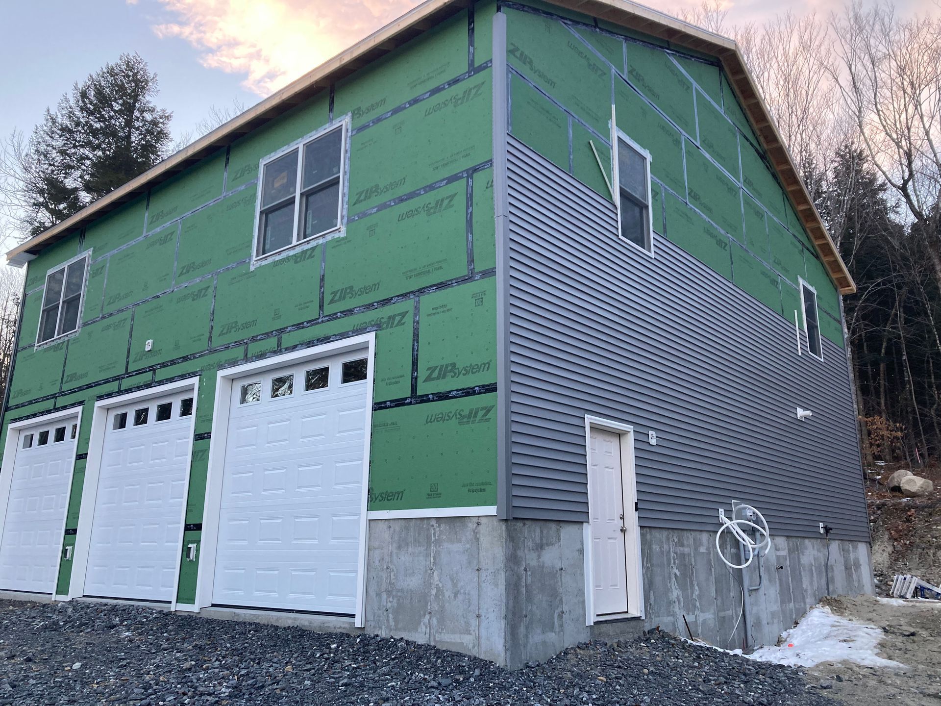 A house is being built with green siding and white garage doors.