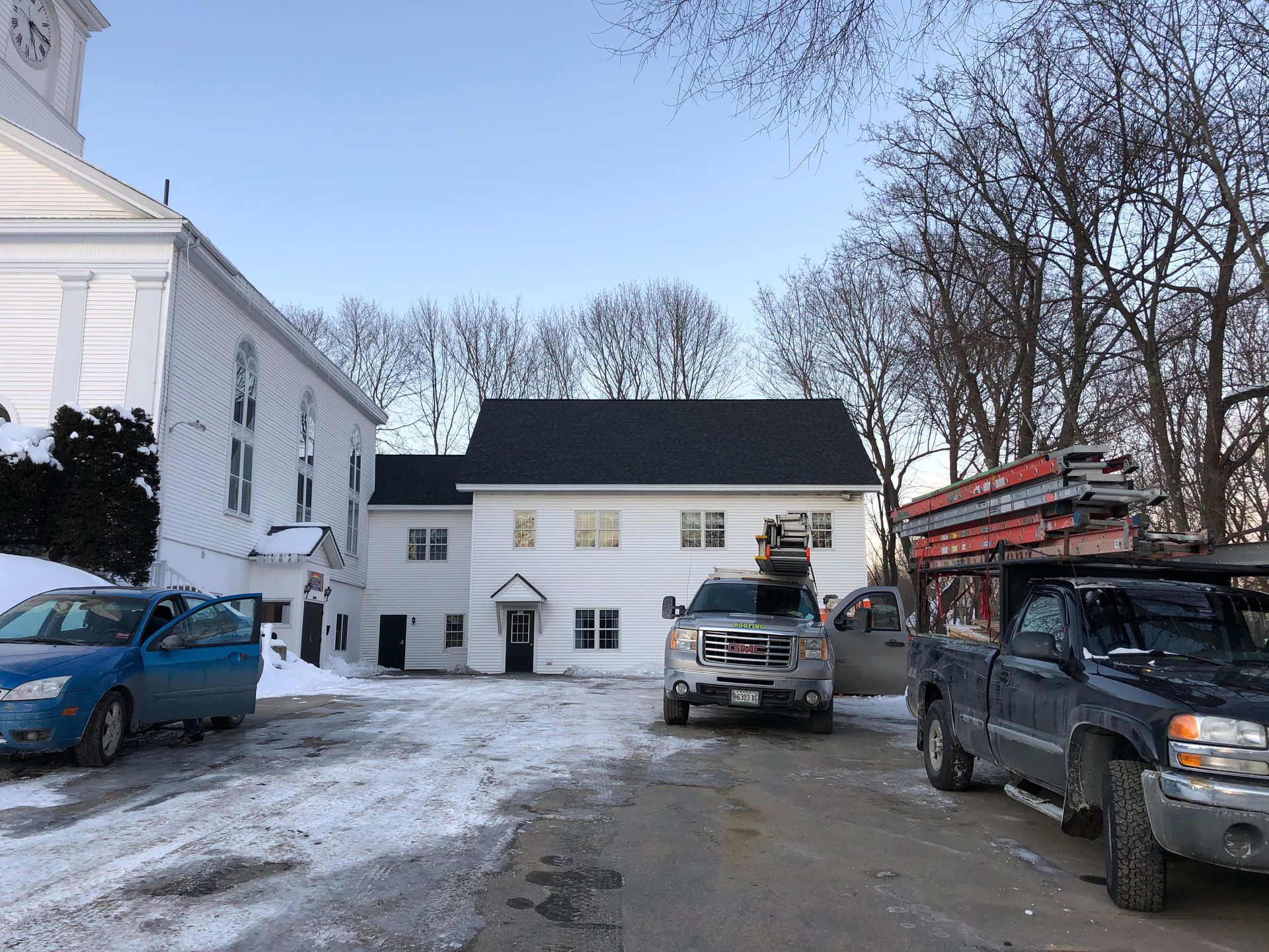 Two trucks are parked in front of a building in the snow.