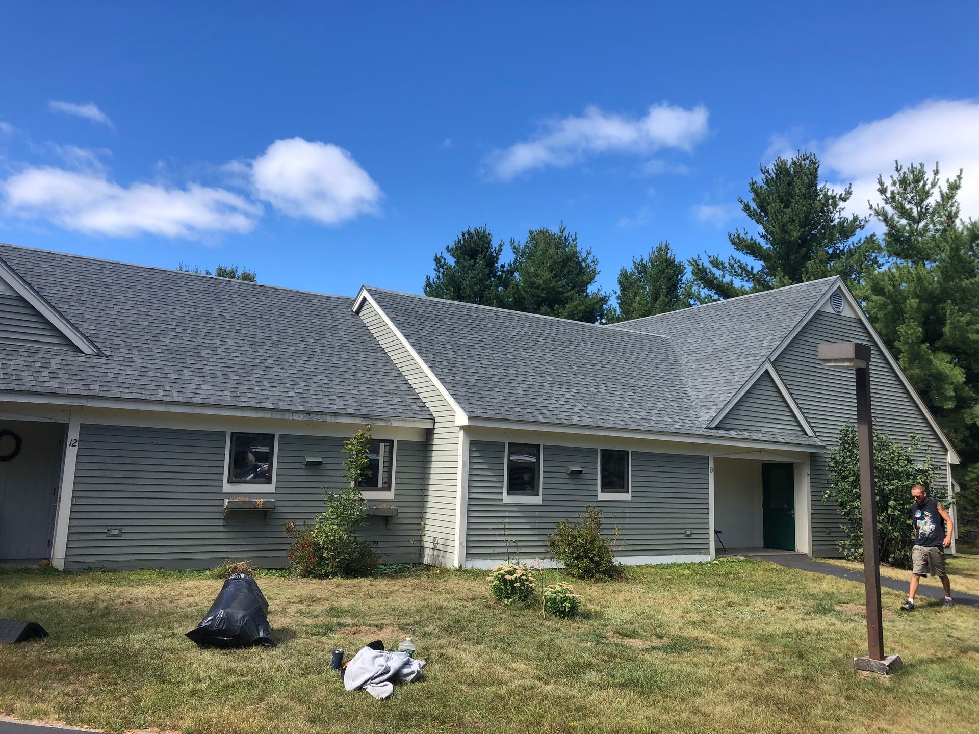 A man is standing in front of a house with a gray roof.