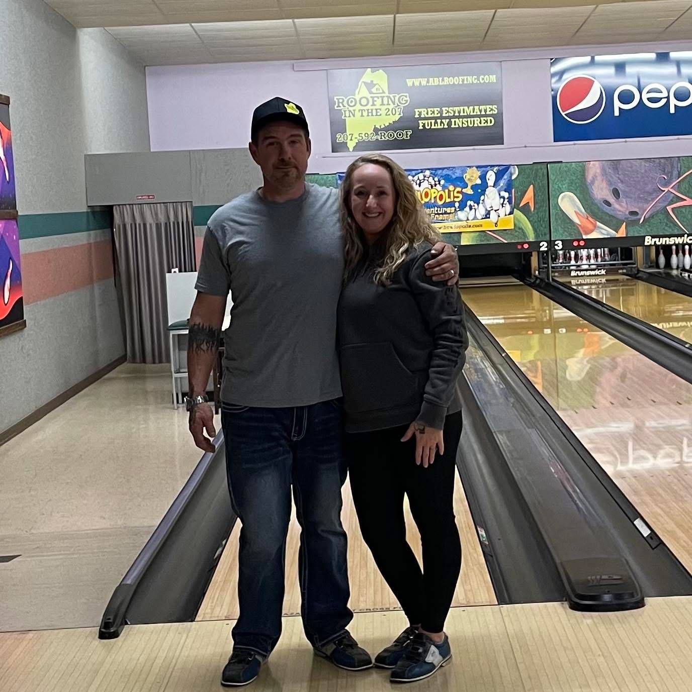A man and a woman are posing for a picture in a bowling alley