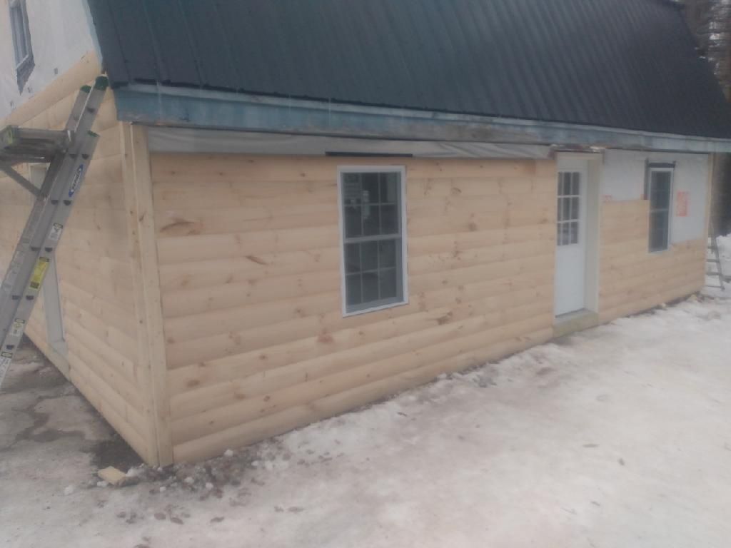 A log cabin with a black roof is being built in the snow.