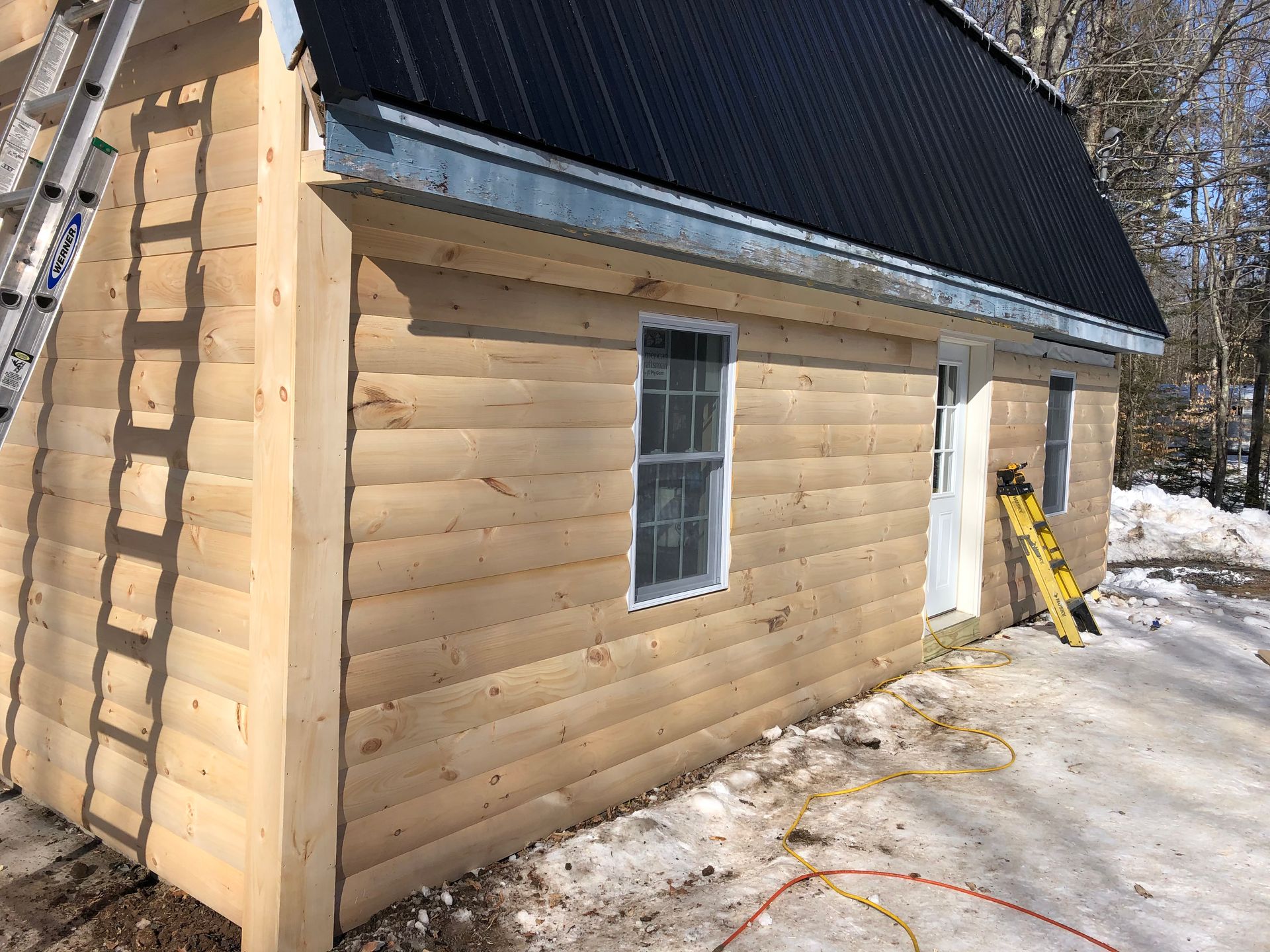 A log cabin with a black roof is being built in the snow.