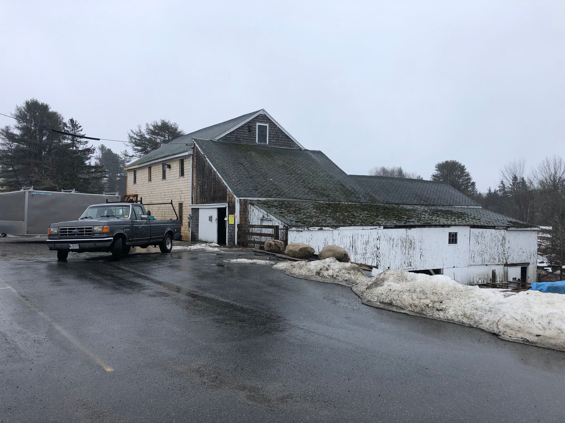 A truck is parked in front of a barn on a snowy day.