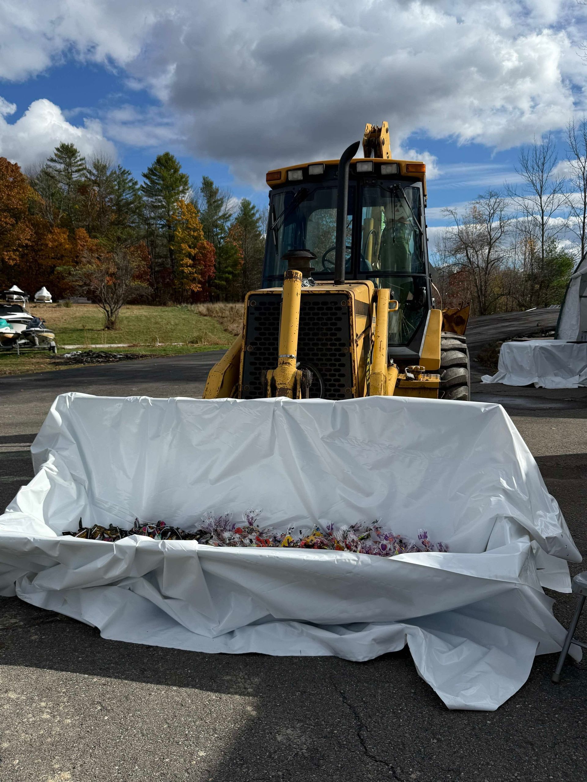 Yellow construction vehicle with white tarp containing flowers, outside on a sunny day.