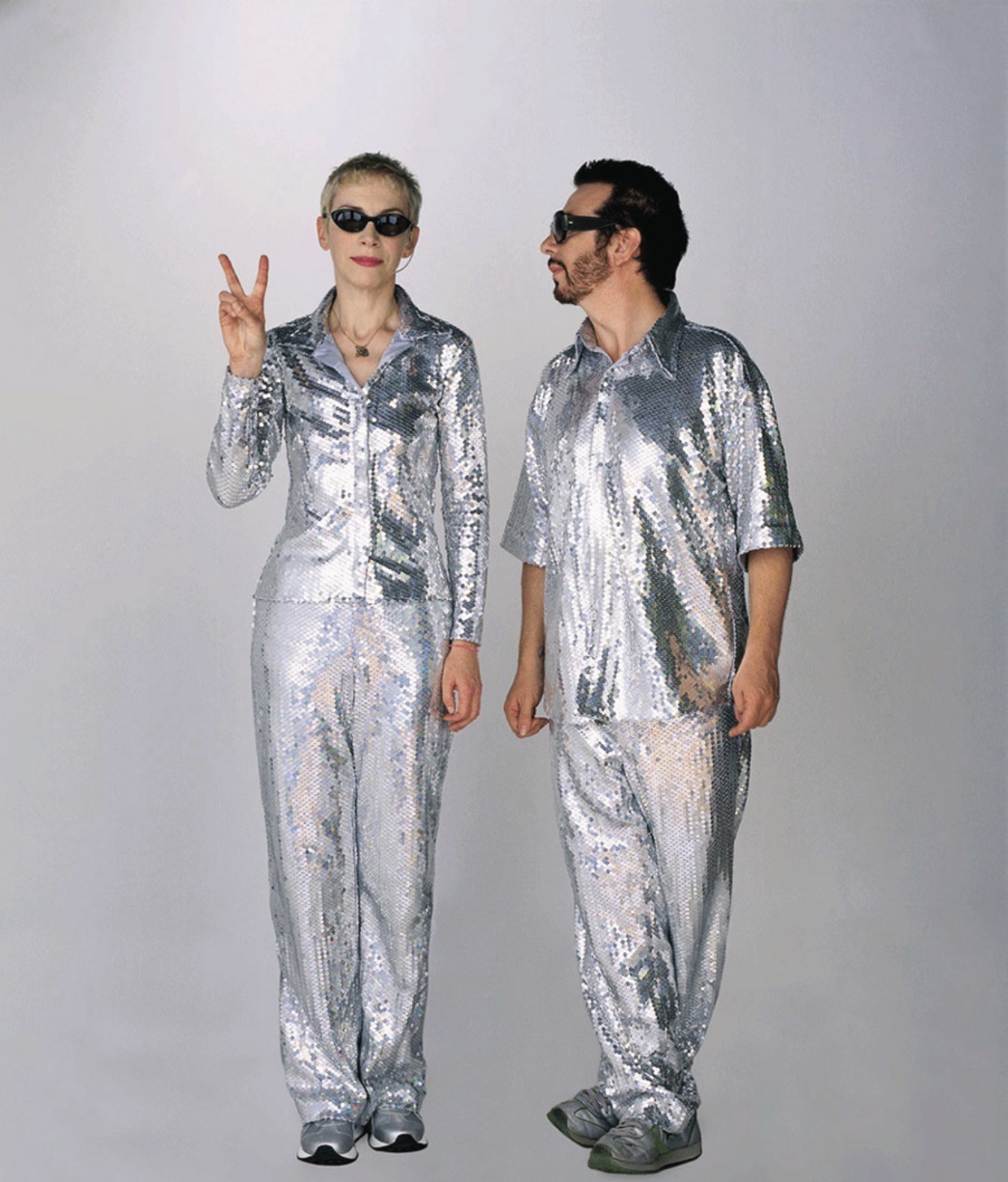 A man and a woman are standing next to each other in silver outfits