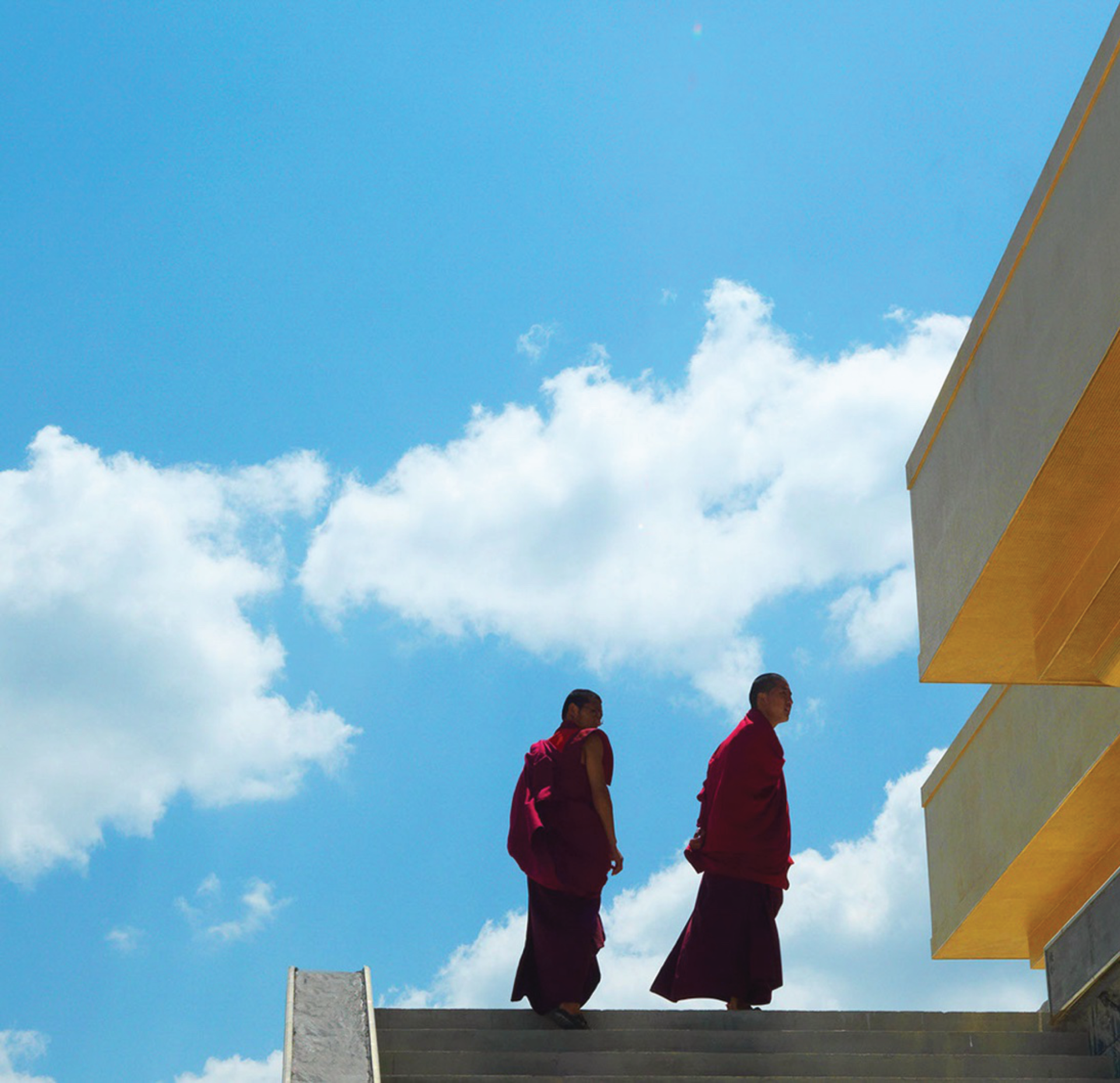 Two monks walking down a set of stairs with a blue sky in the background