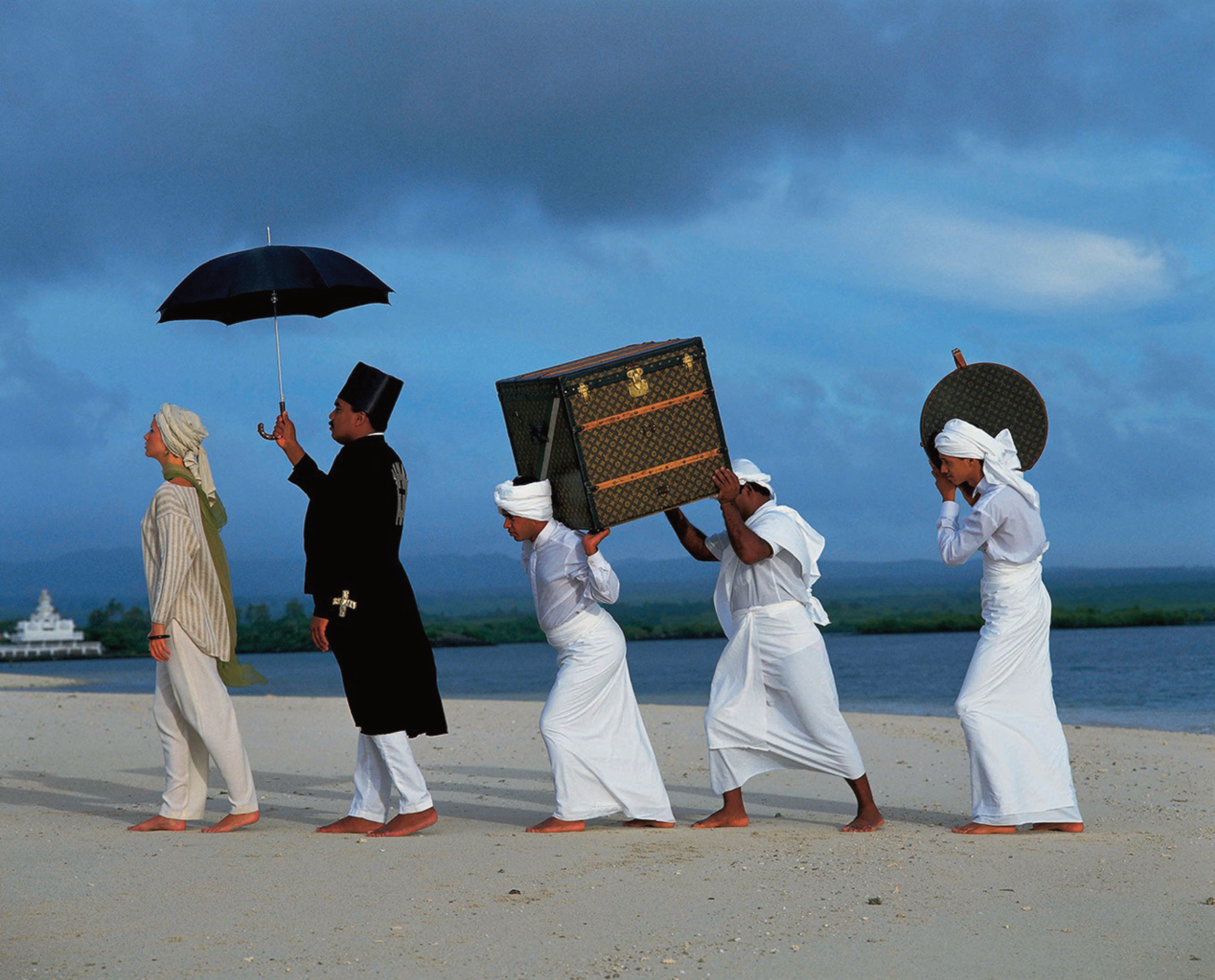 A group of people carrying a trunk and umbrellas on a beach