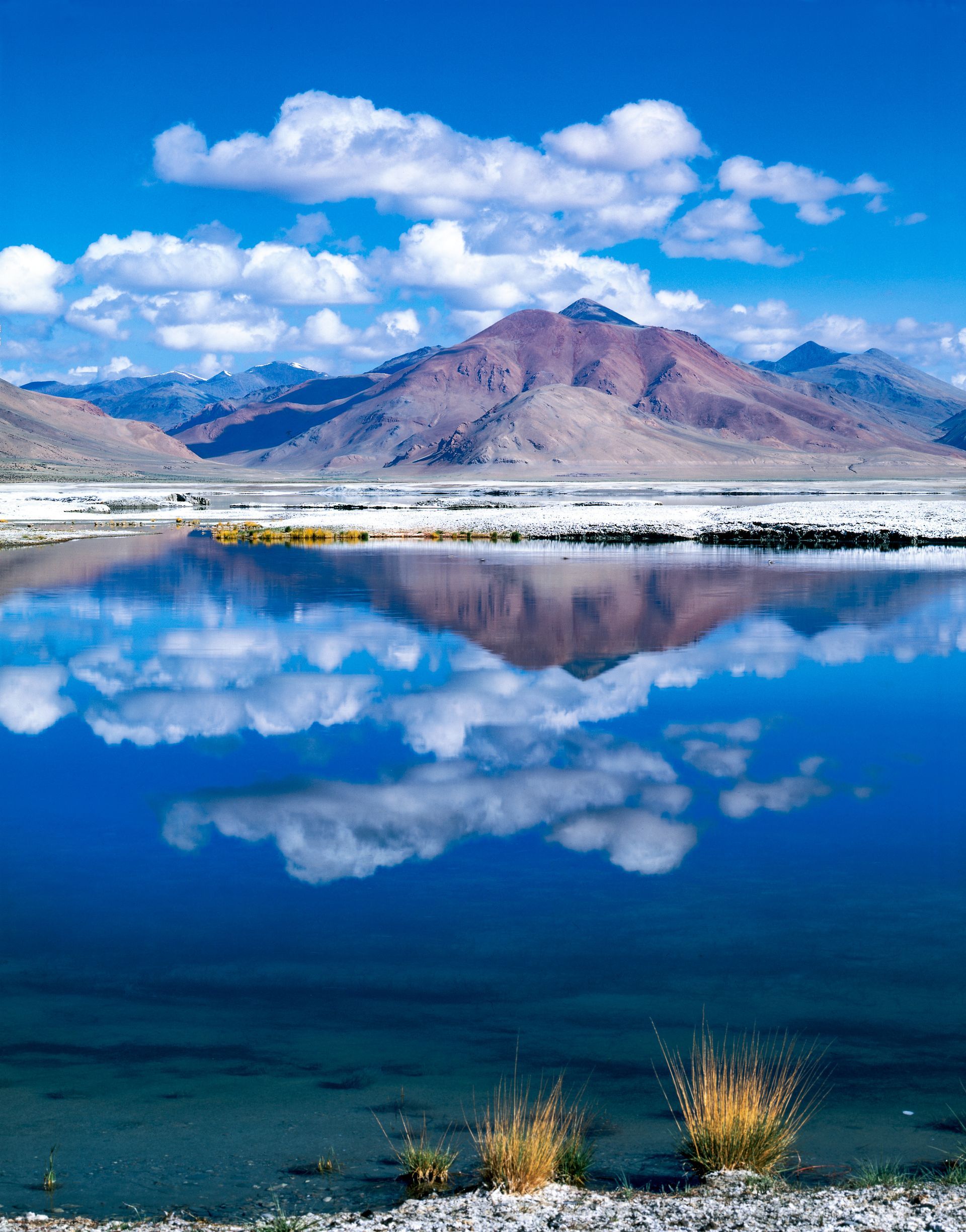 A lake with mountains in the background and clouds reflected in the water