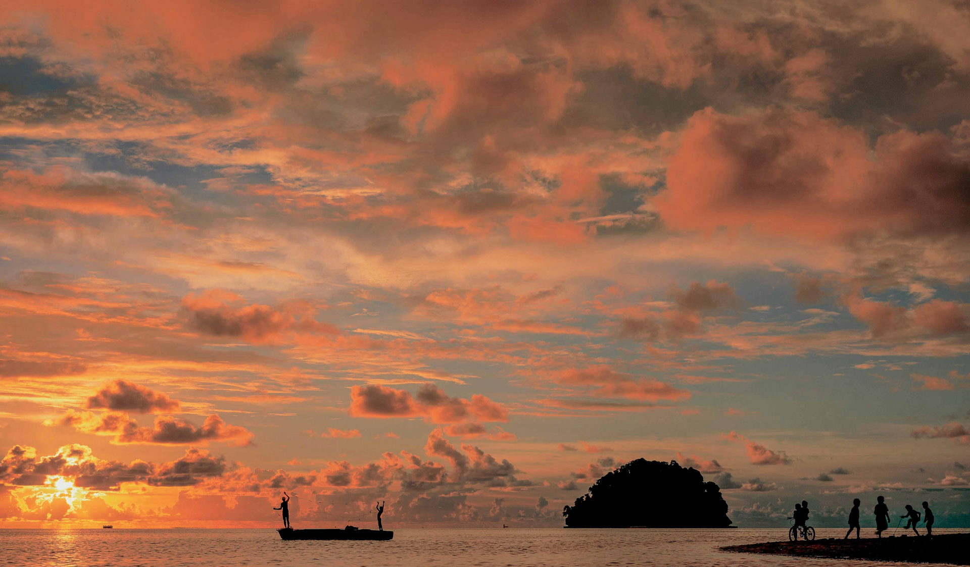 A group of people are standing on a beach at sunset.