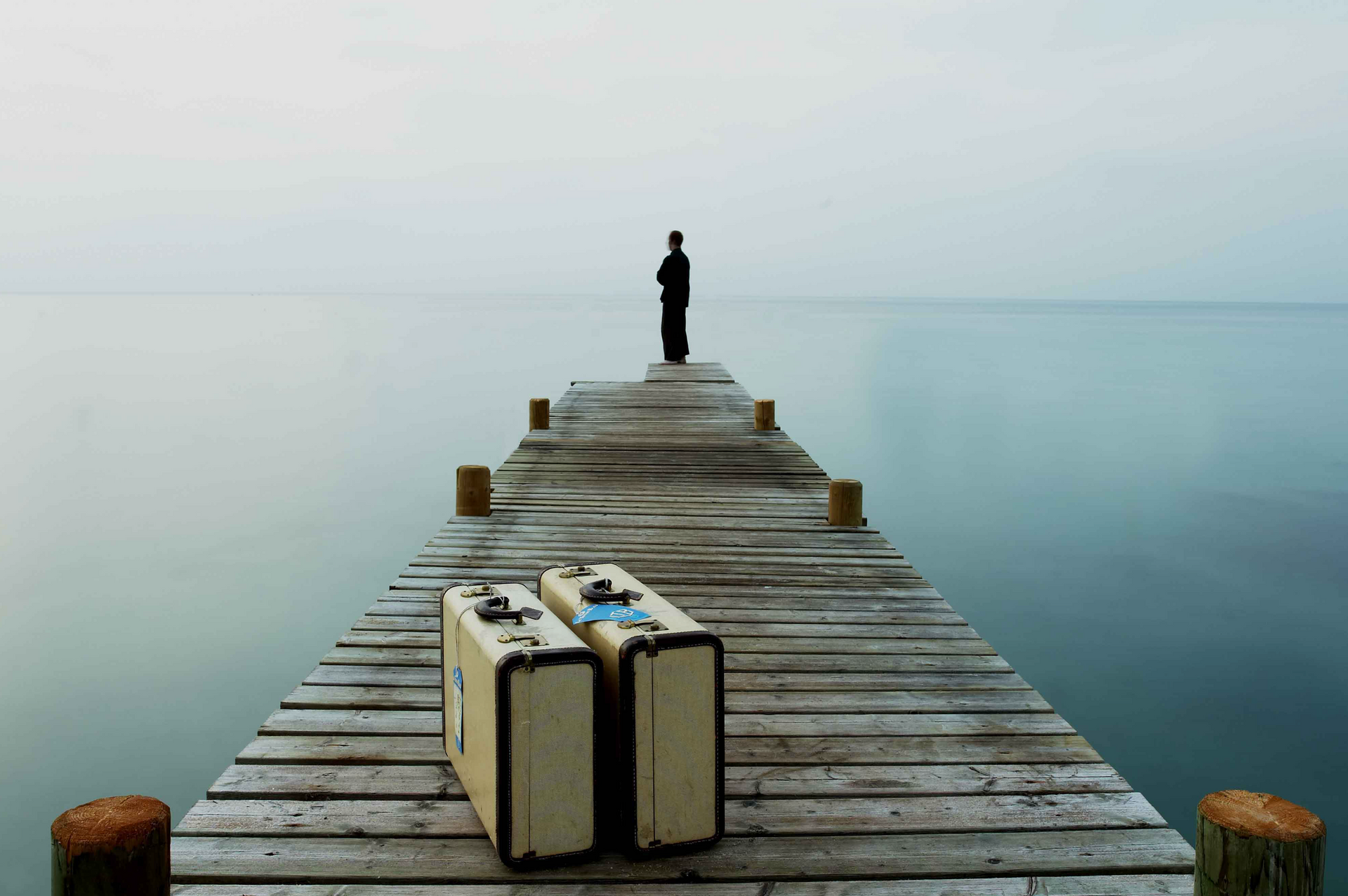 A man is standing on a pier with two suitcases on it