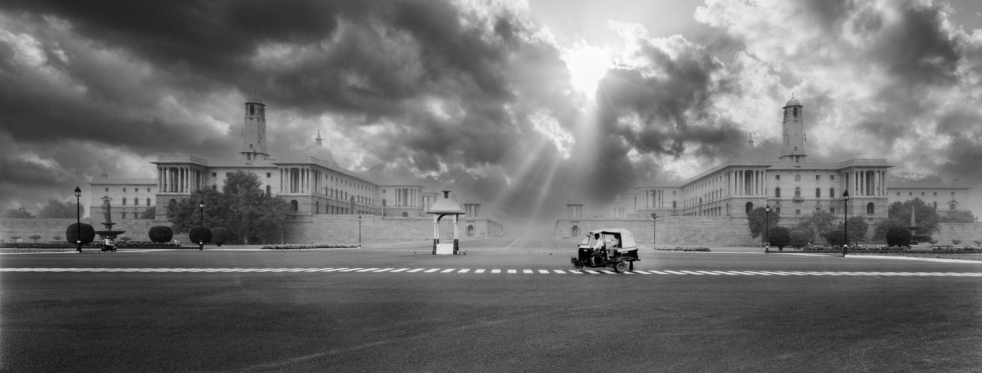A black and white photo of a large building with the sun shining through the clouds.