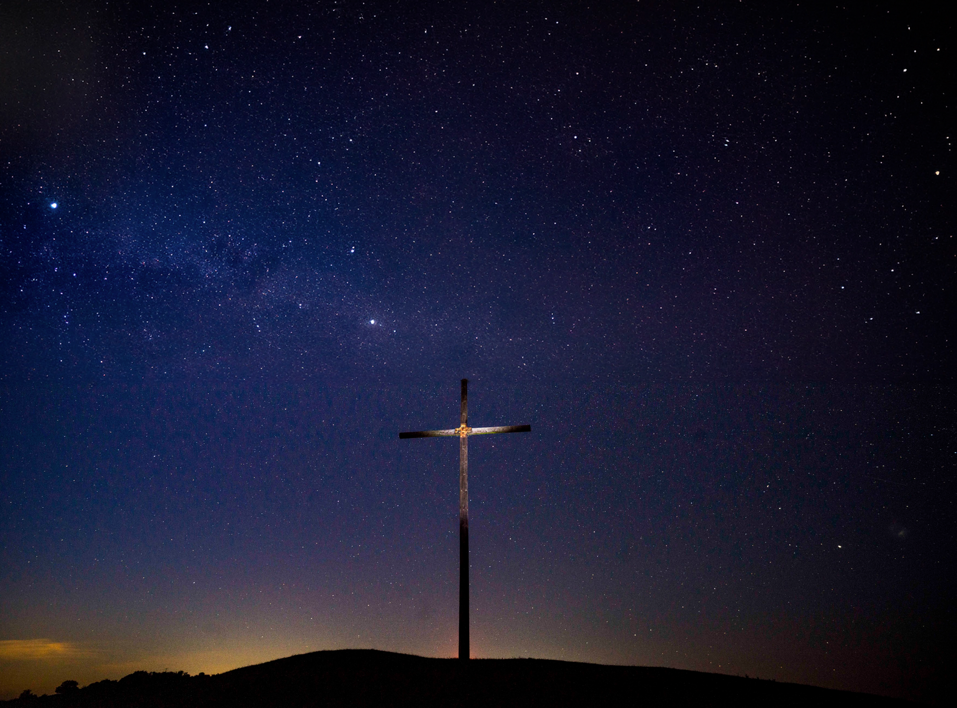 A cross on top of a hill with a starry sky in the background.