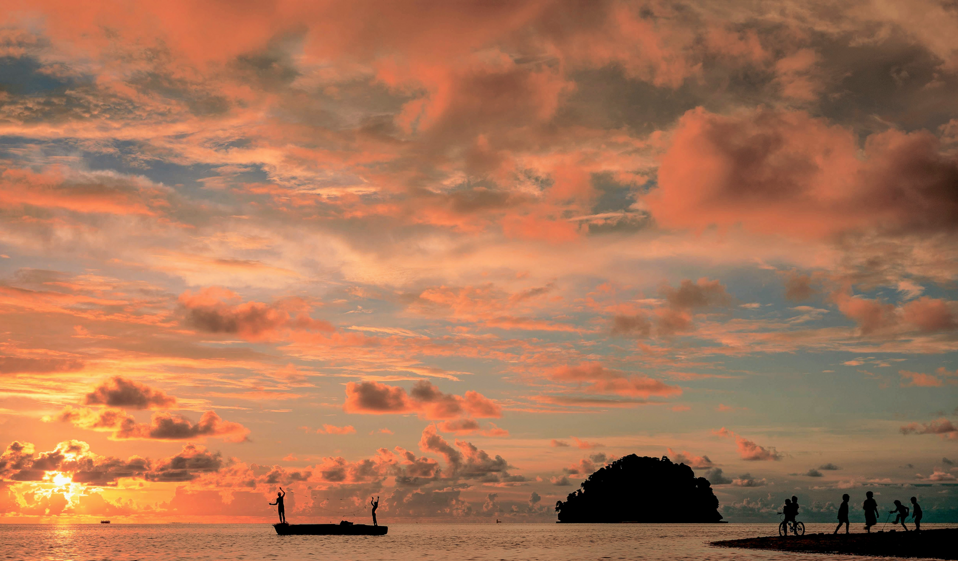 A group of people are standing on a beach at sunset.