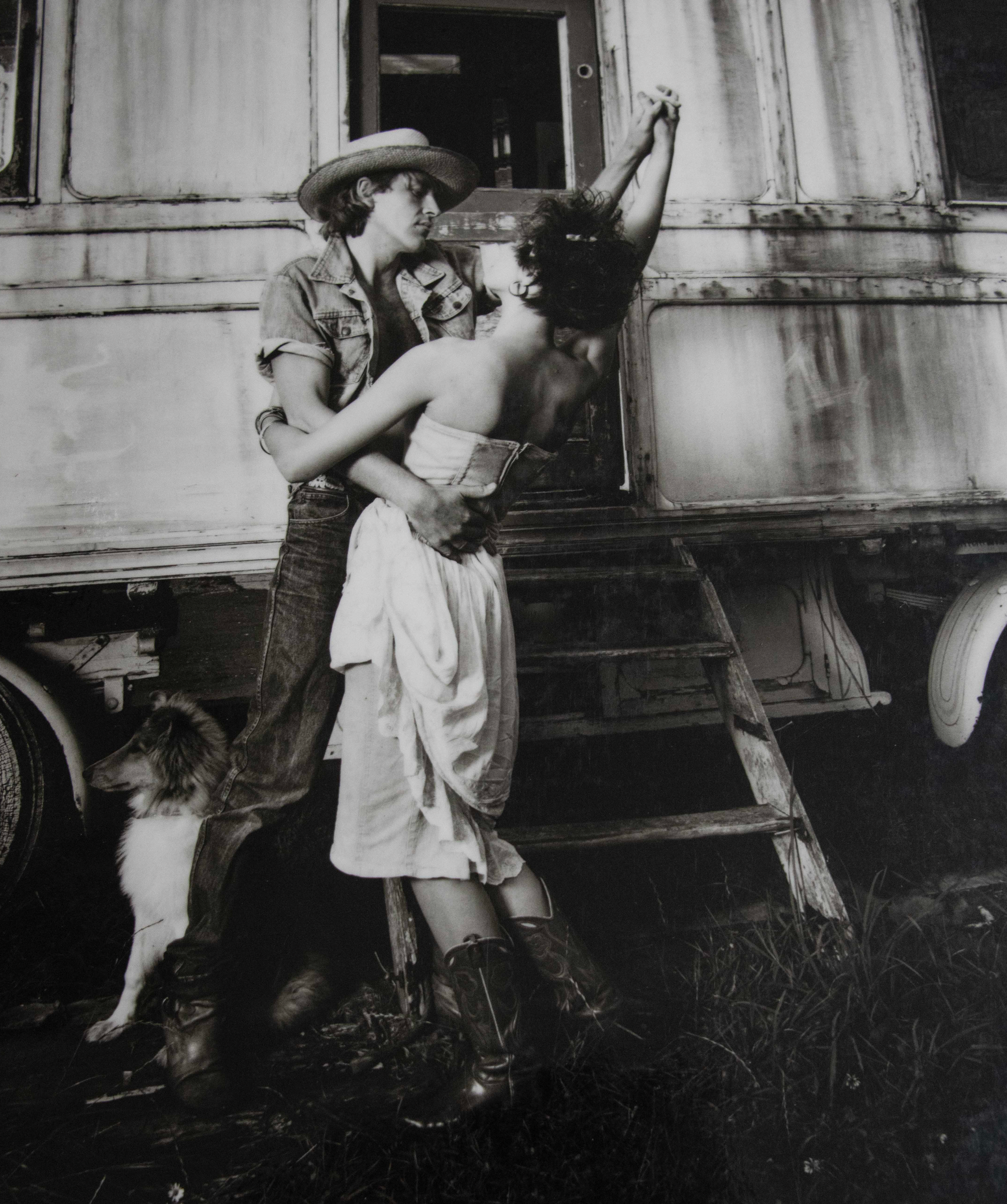 A black and white photo of two people hugging in front of a trailer