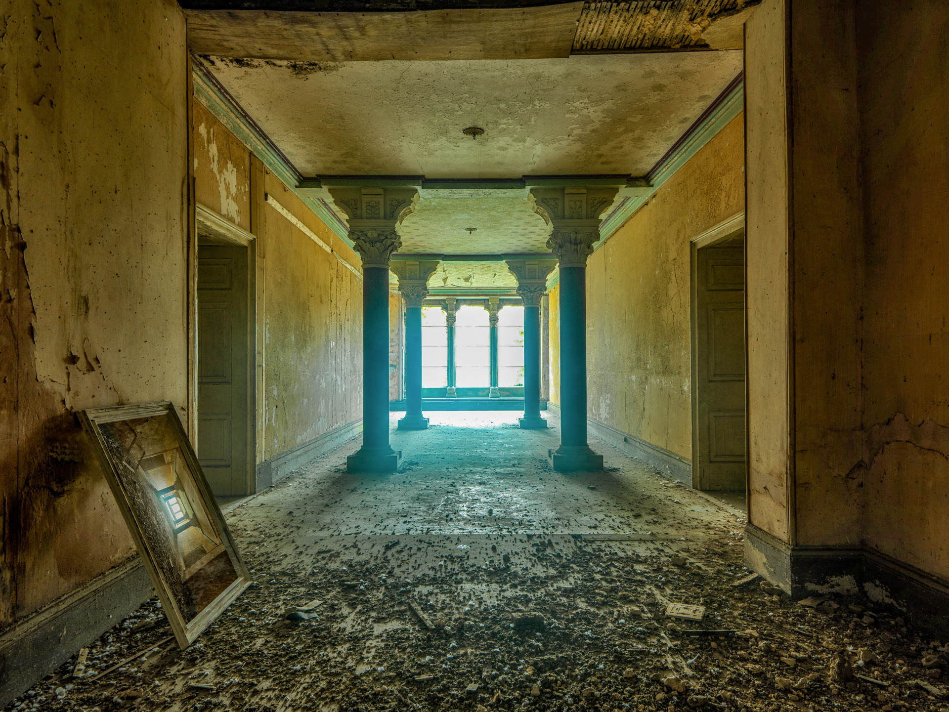 A long hallway in an abandoned building with columns and a window.