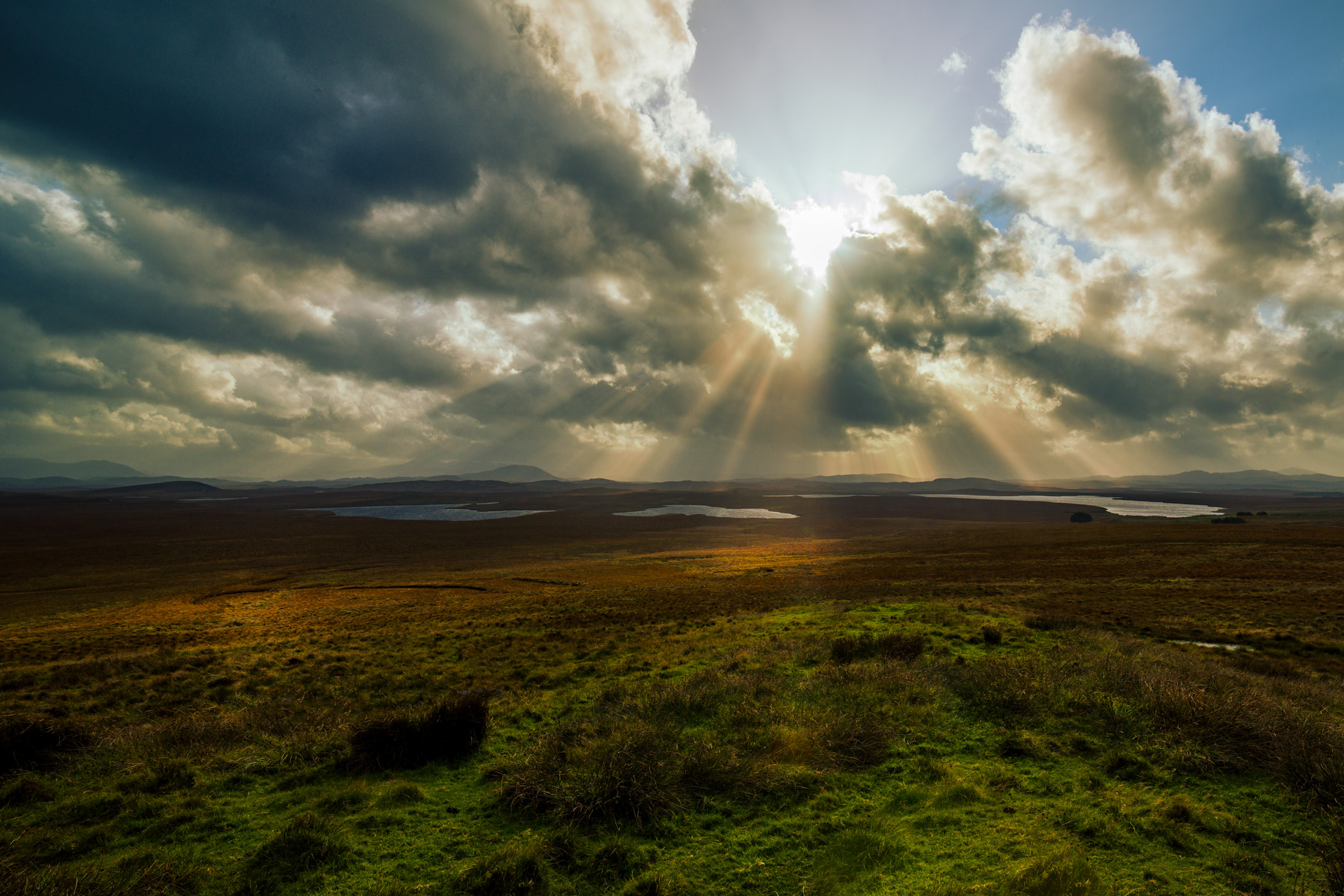 The sun is shining through the clouds over a grassy field.