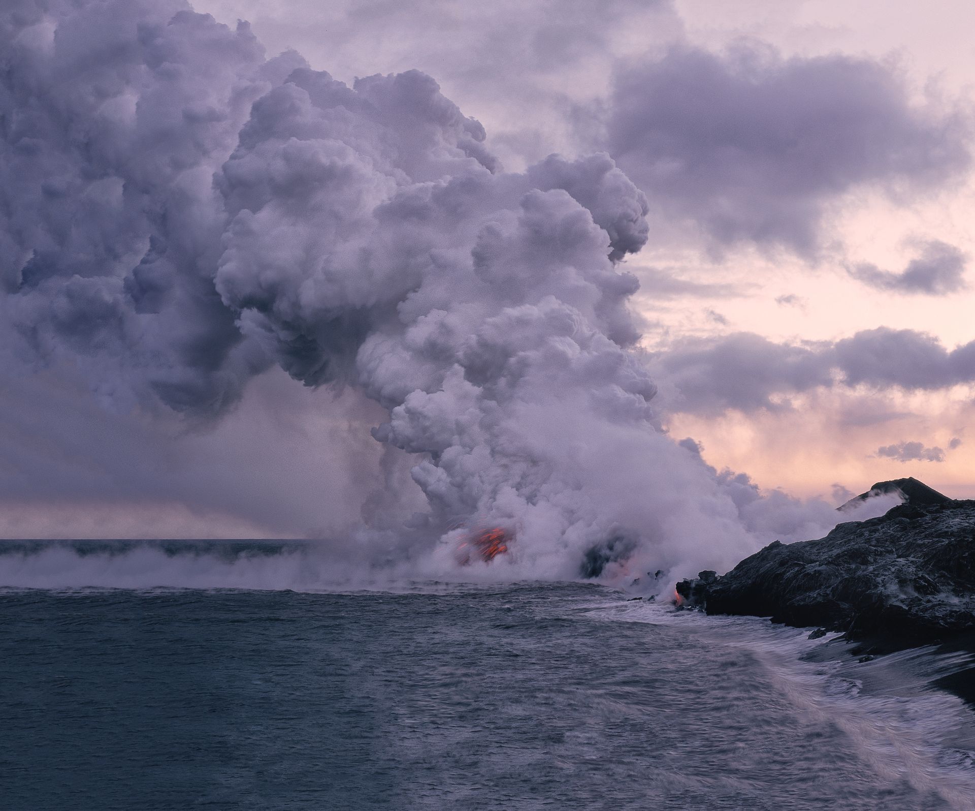 A volcano is erupting into the ocean at sunset.