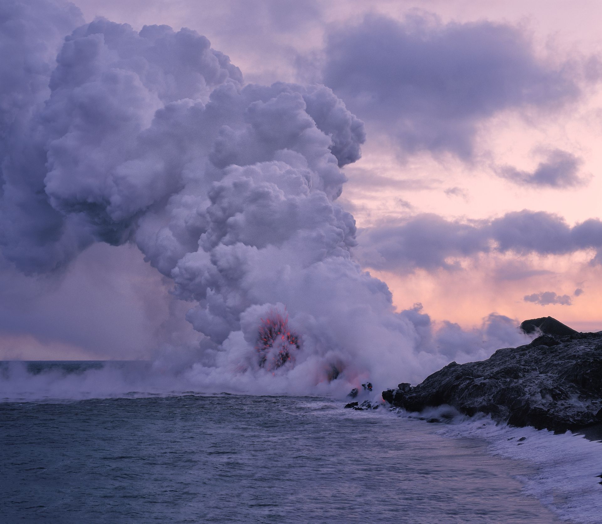 A volcano is erupting into the ocean at sunset