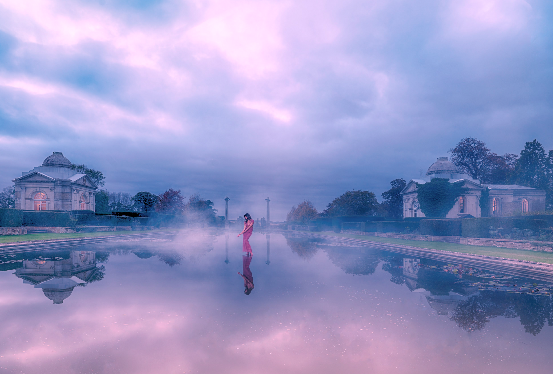 A woman in a pink dress is standing on a bridge over a river.