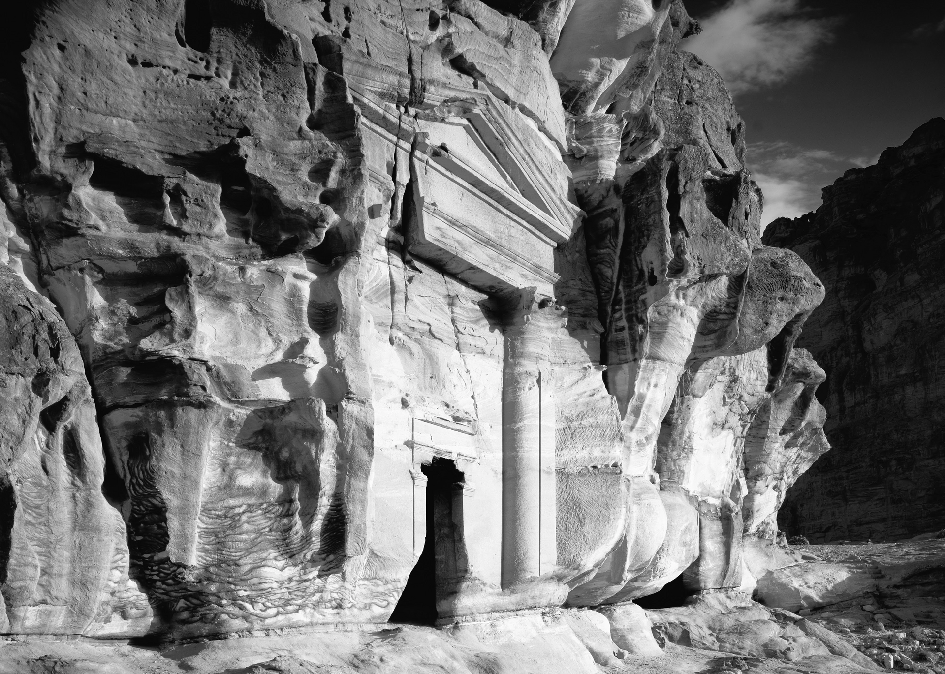 A black and white photo of a cave in the middle of a mountain.