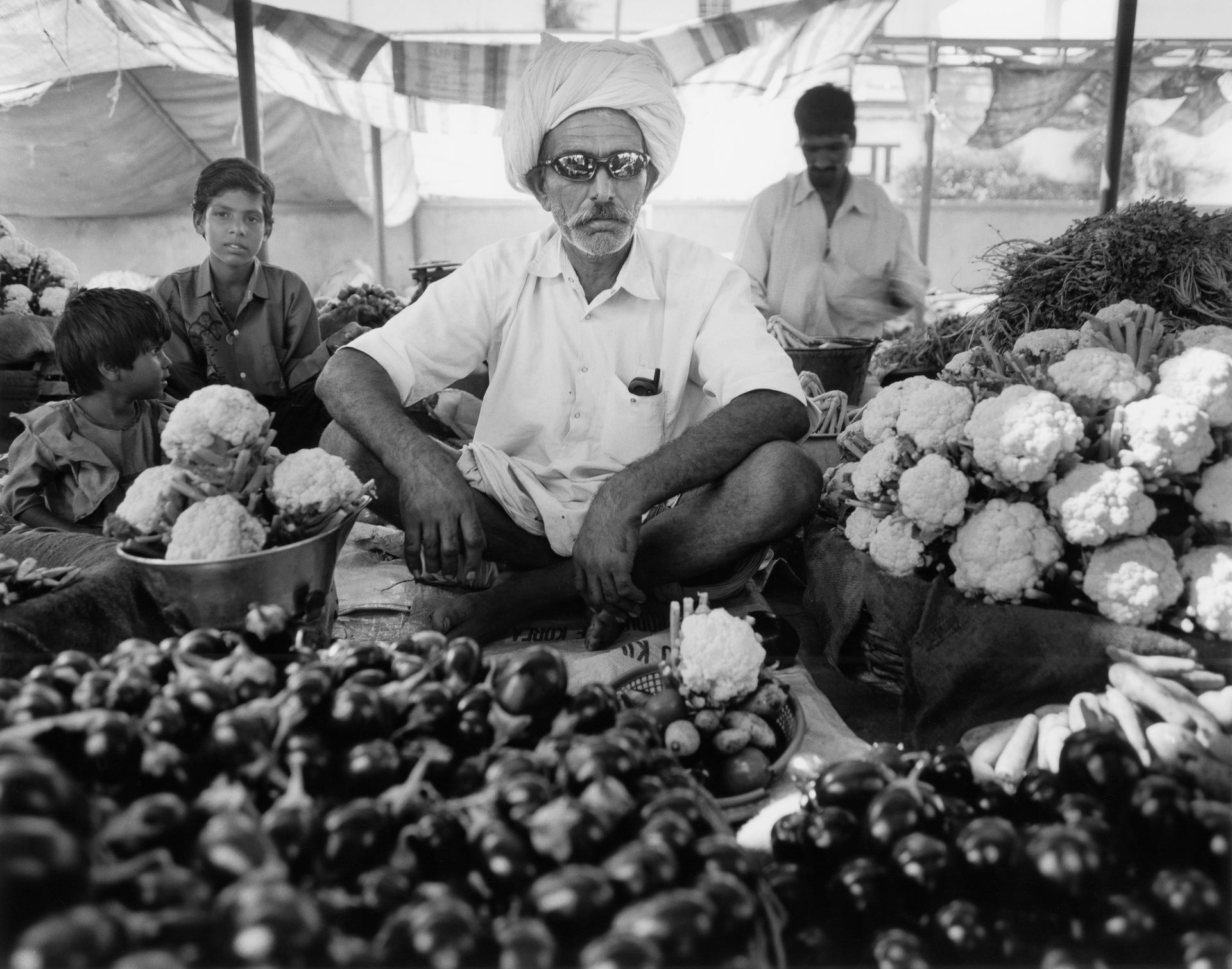 A man is sitting in front of a table full of vegetables.
