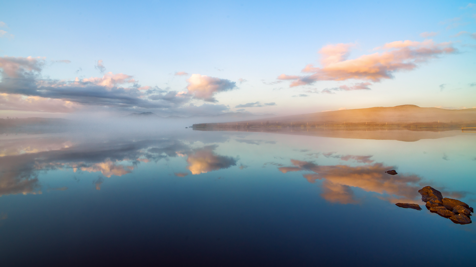 A lake with mountains in the background and clouds reflected in the water.