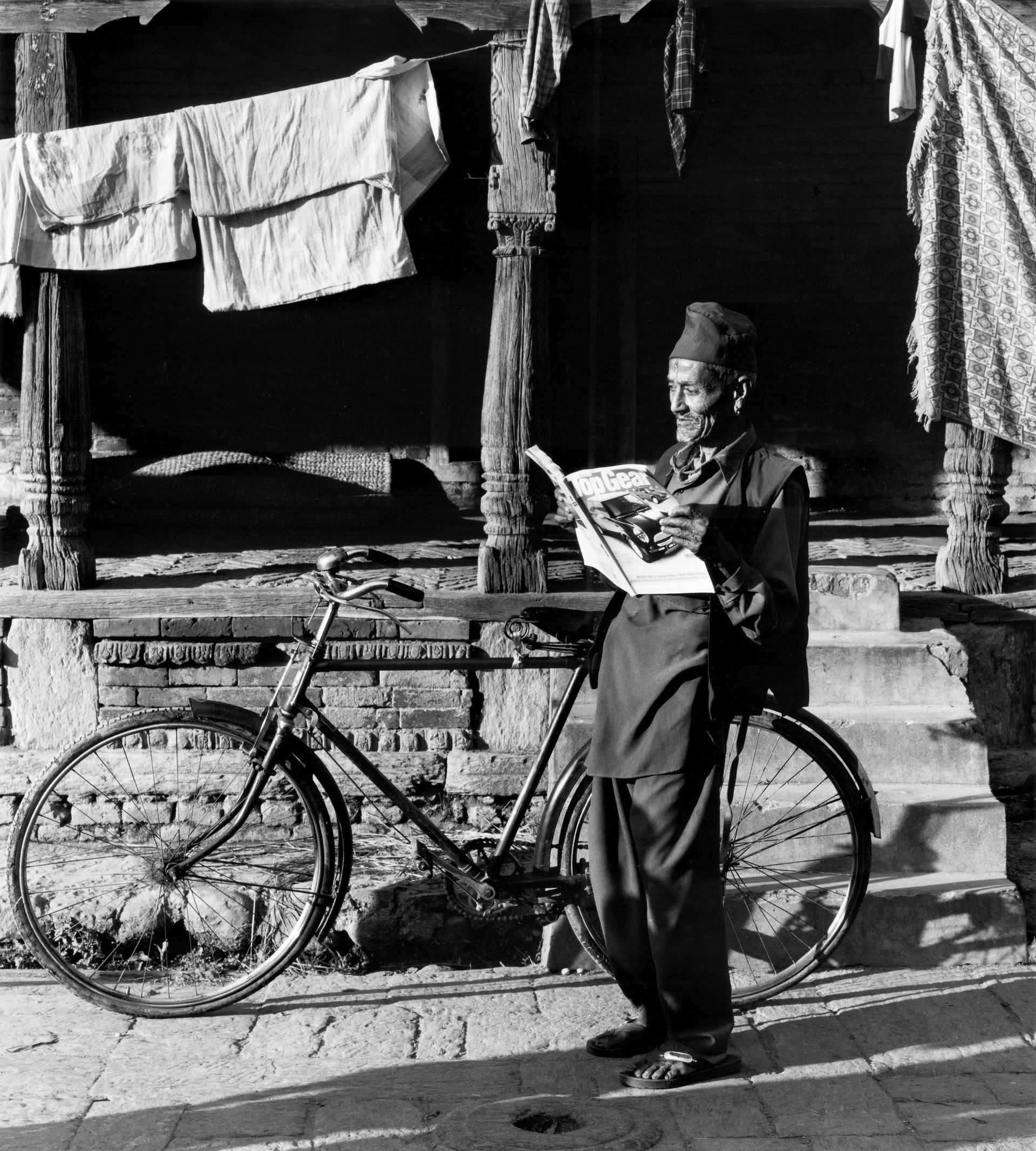 A man is standing next to a bicycle reading a book.