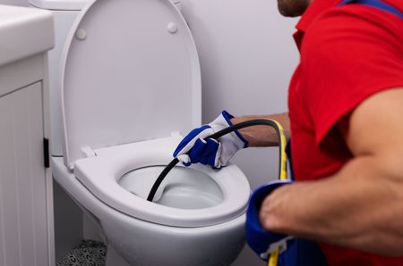 MDM Plumbing & Sewer LLC | A man is cleaning a toilet with a hose.