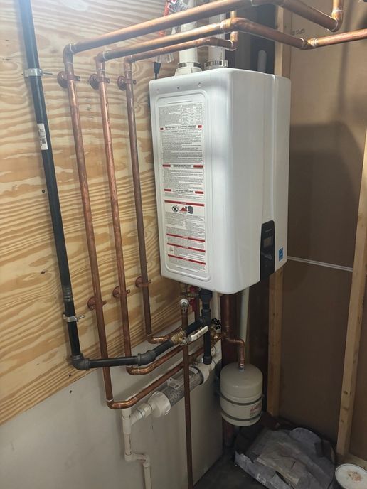 A white tankless water heater installed on a wooden wall with copper pipes and black gas pipe.