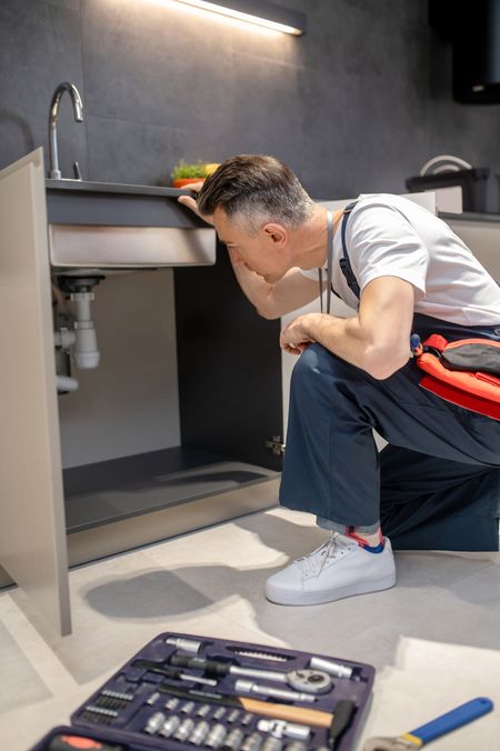 MDM Plumbing & Sewer LLC | A man is kneeling down under a sink in a kitchen.