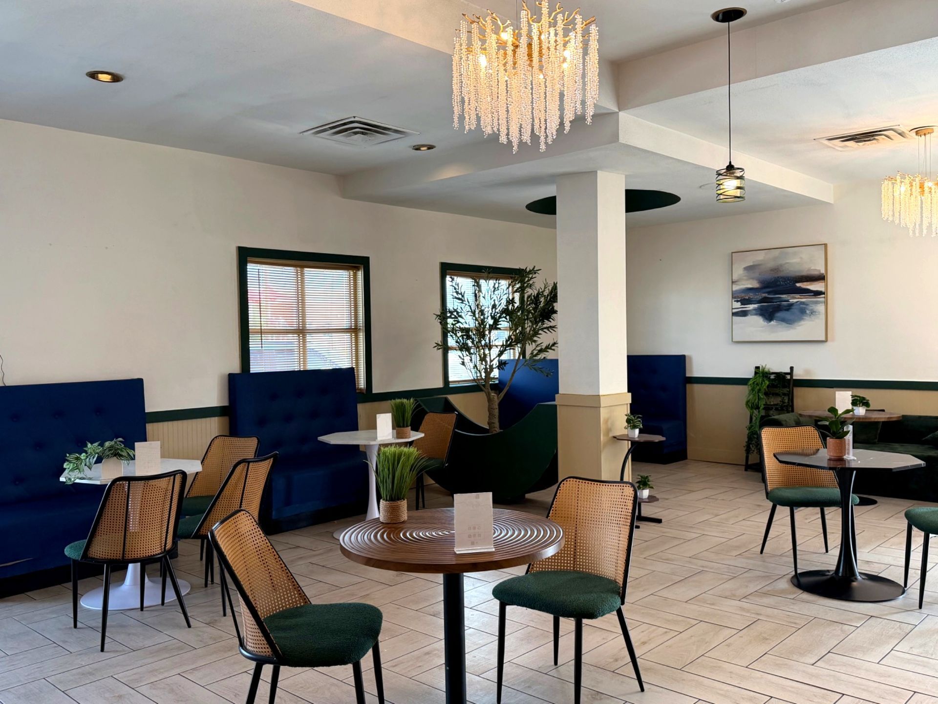 Modern lounge with blue booths, wicker chairs, tables, and a chandelier in a bright, airy room