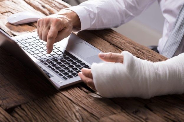 A man with a cast on his arm is using a laptop computer.