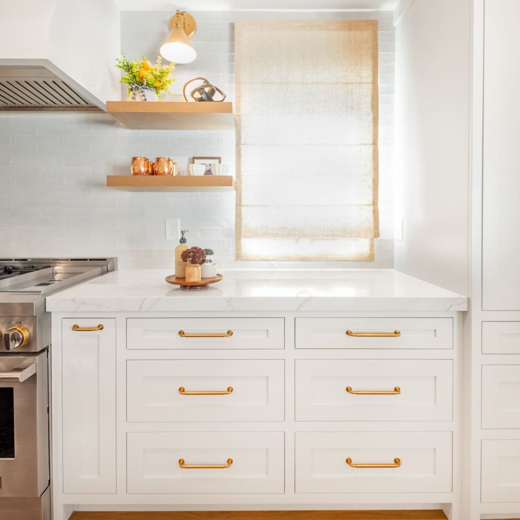 A kitchen with white cabinets , a stove , and a window.