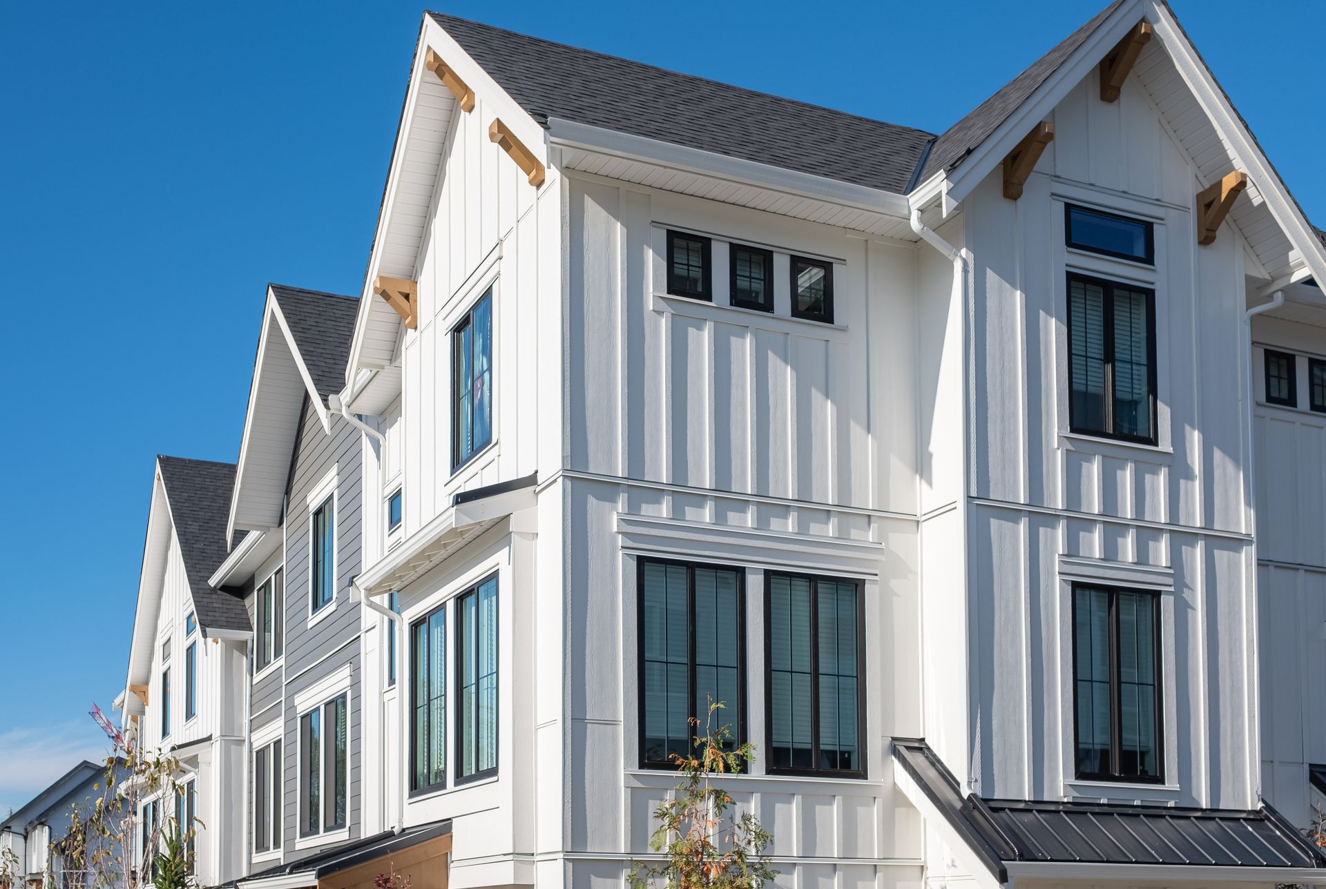 New modern townhome with white siding, black‑framed windows, and gabled roofs under blue sky