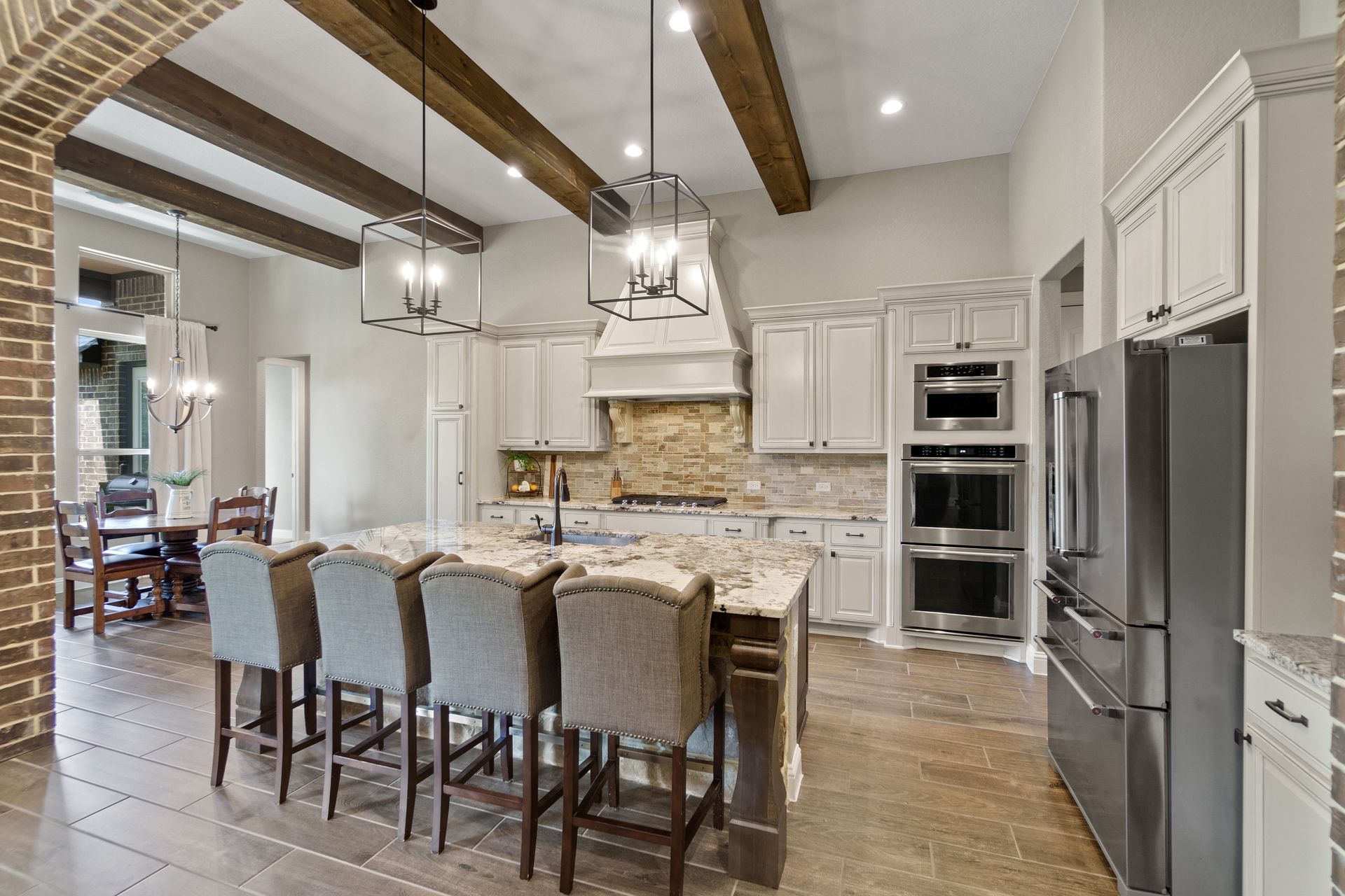 Upscale kitchen with granite island, pendant lights, and rustic ceiling beams.