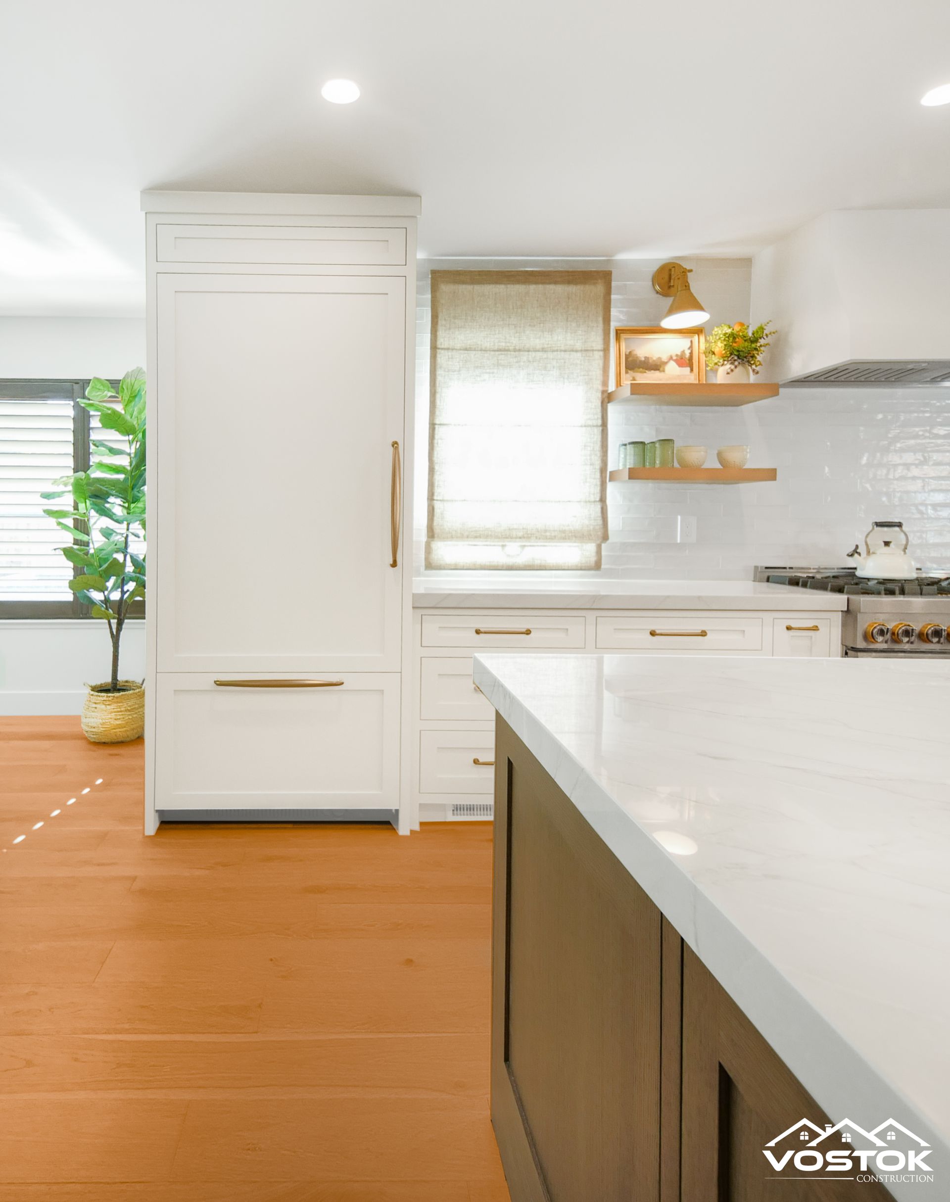 Bright kitchen with white cabinets, gold hardware, wood floating shelves, and natural woven shade