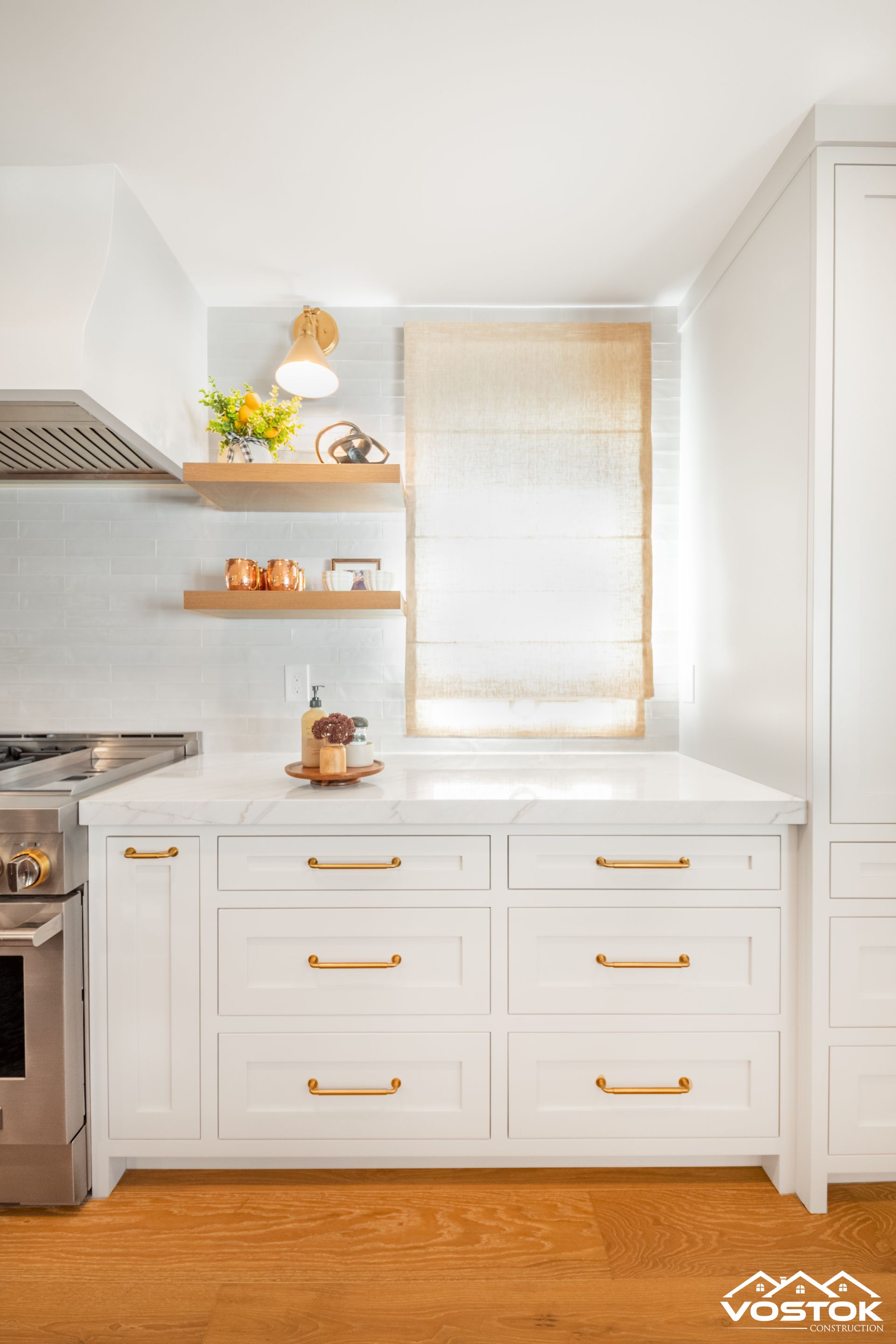 A kitchen with white cabinets , a stove , a sink , and a window.
