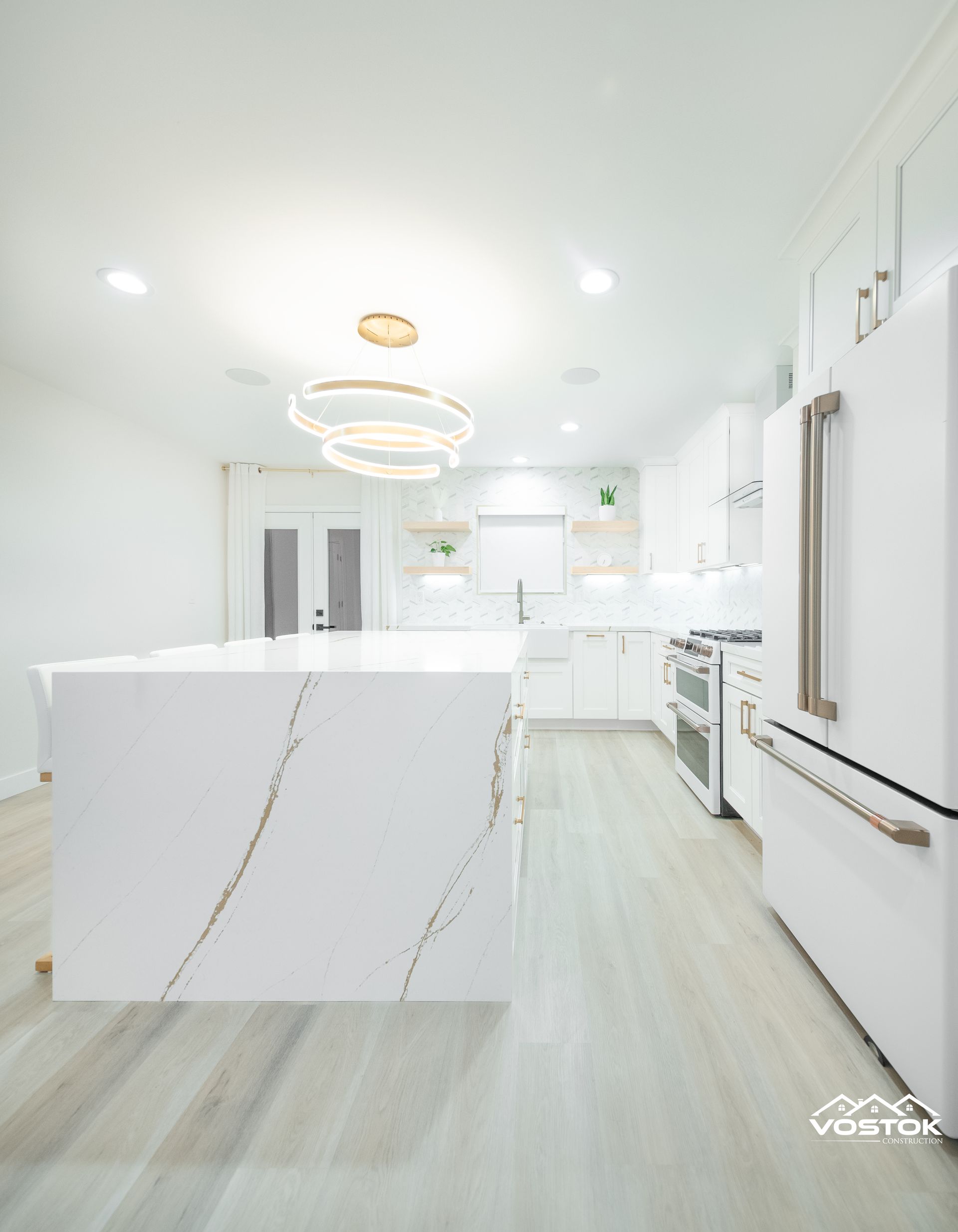 A kitchen with white cabinets , a large island , a refrigerator and a stove.
