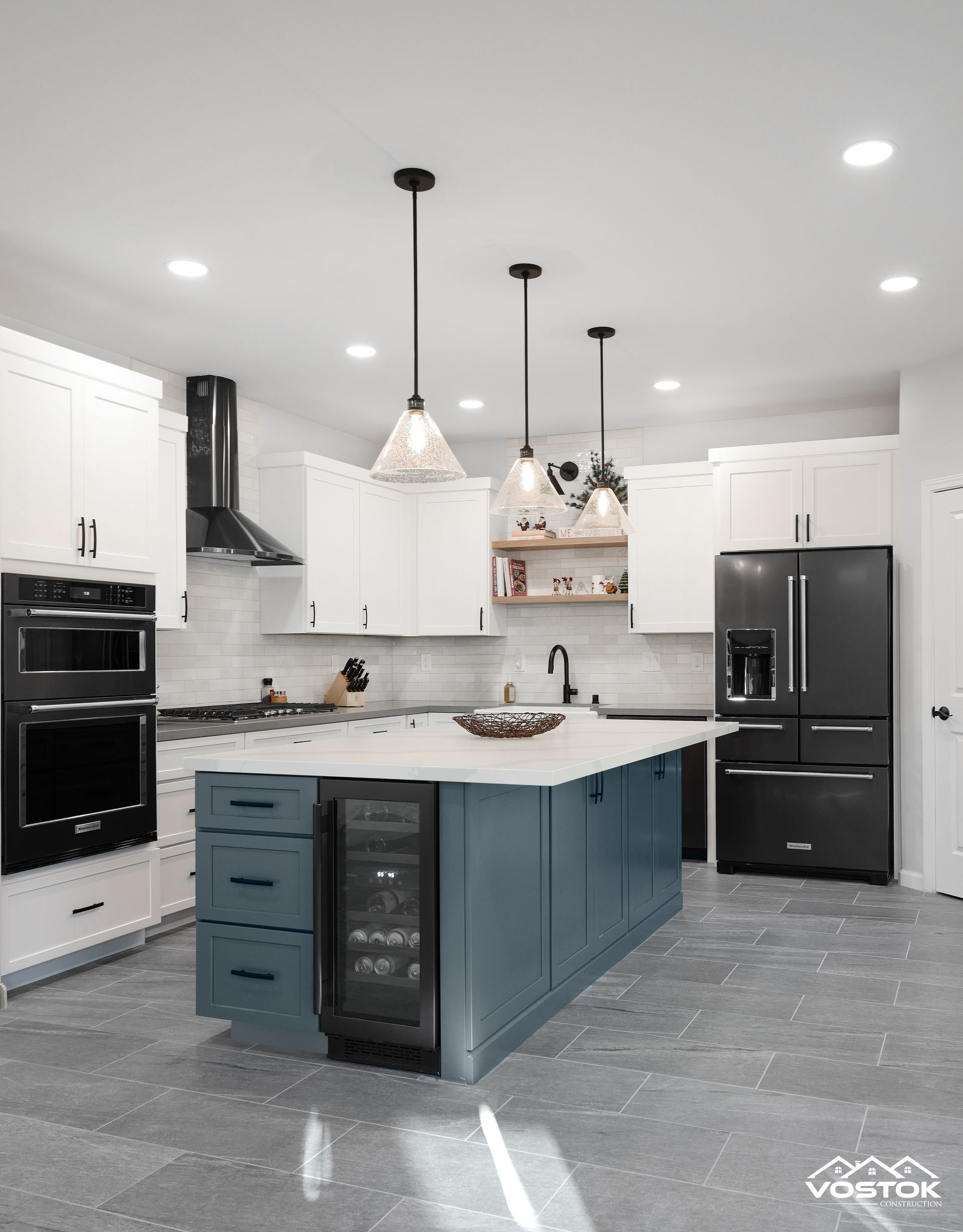 A kitchen with blue cabinets , white cabinets , black appliances and a large island.