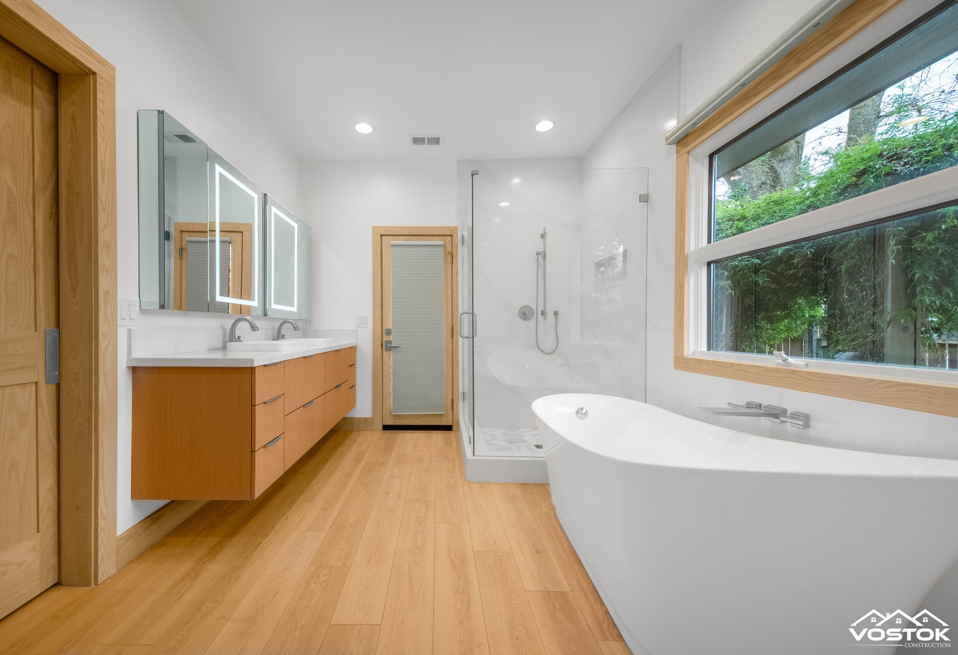 A bathroom with two sinks , a tub , a shower and a window.