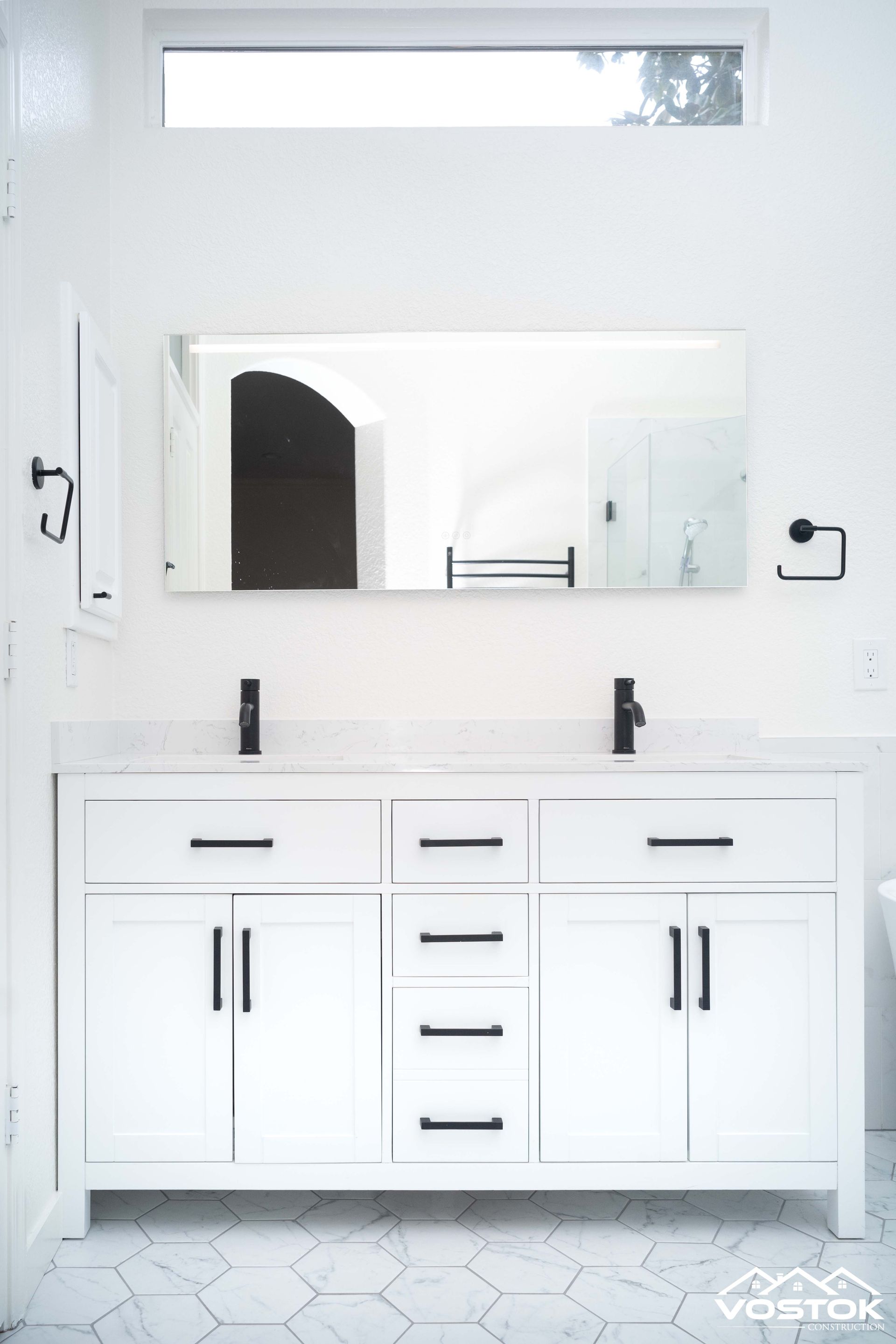 A bathroom with two sinks , a mirror and a window.
