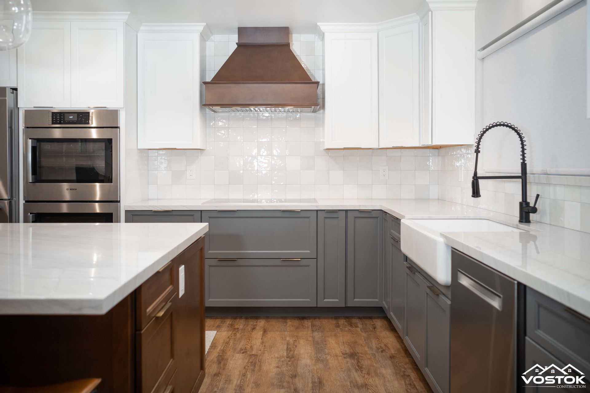 A kitchen with gray cabinets , white counter tops , stainless steel appliances and a sink.