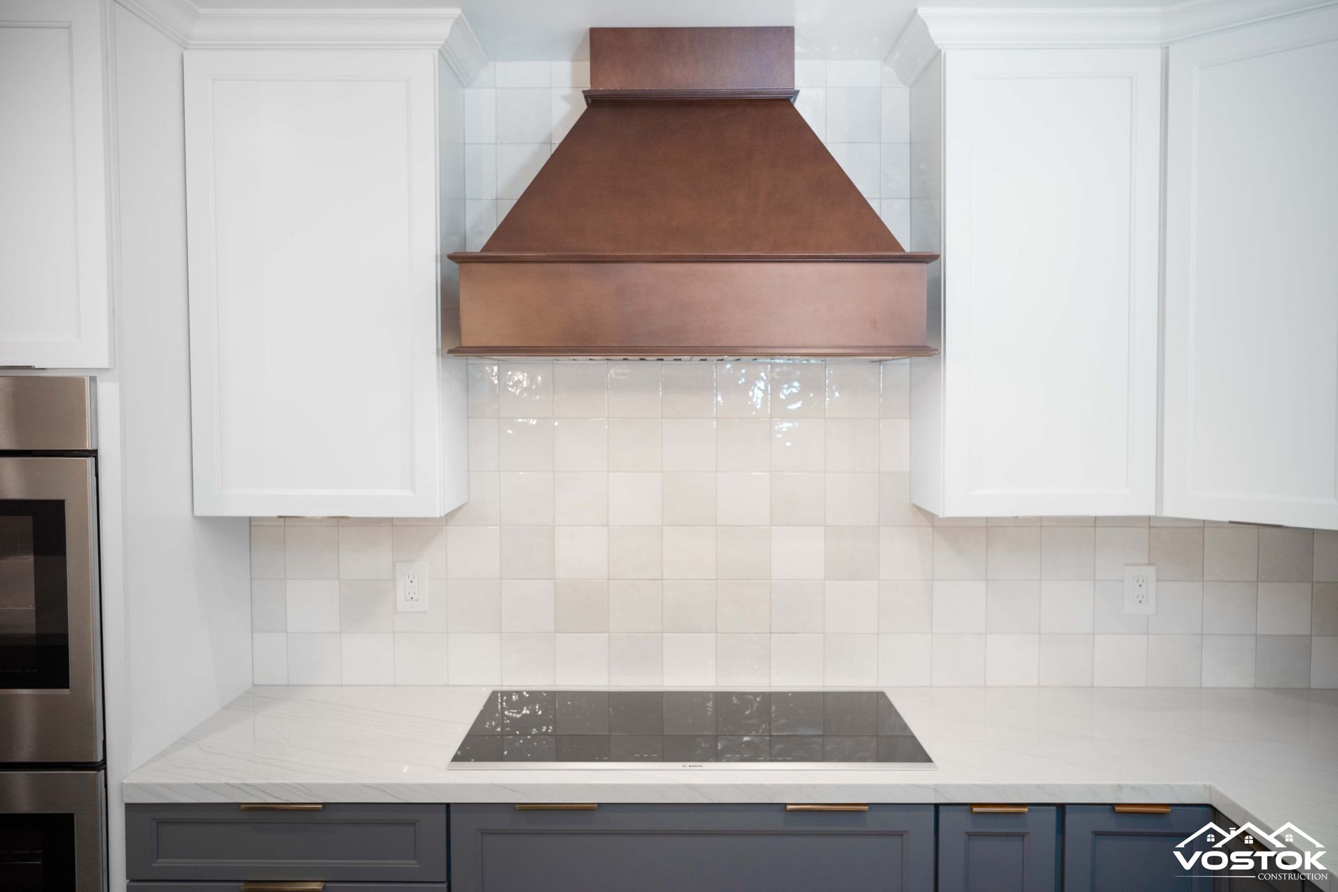 A kitchen with white cabinets and a copper hood above the stove.