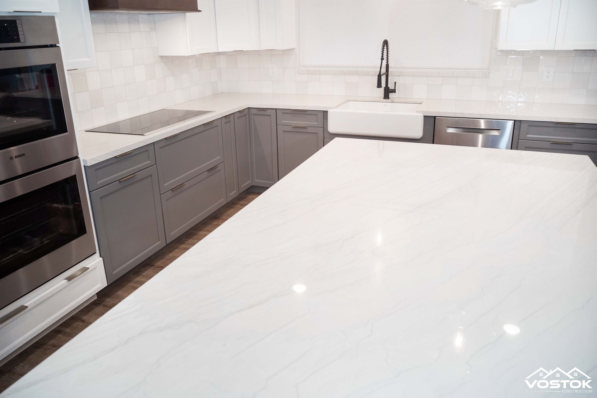 A kitchen with gray cabinets , white counter tops , stainless steel appliances and a large island.