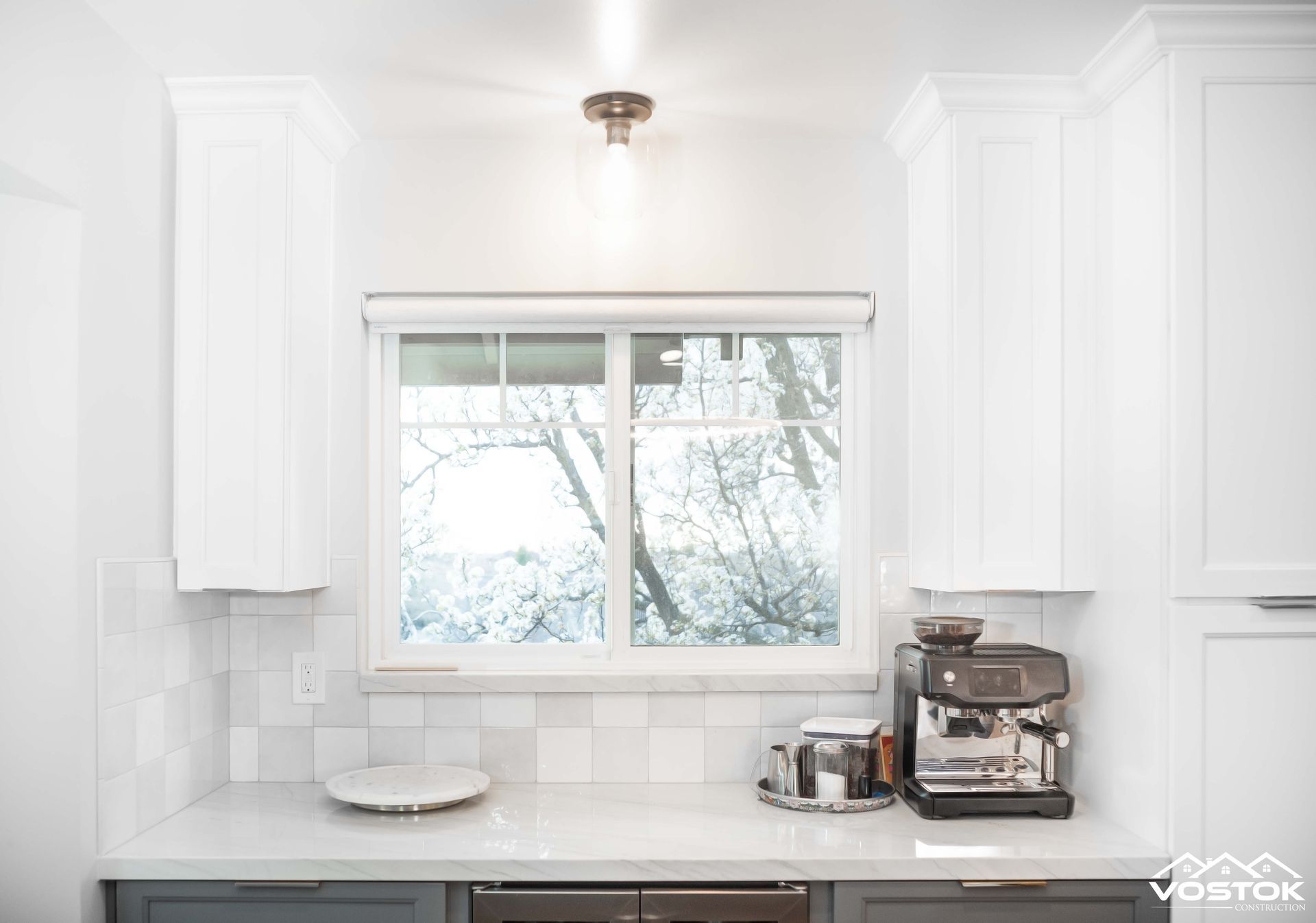 A kitchen with white cabinets , a coffee maker , and a window.