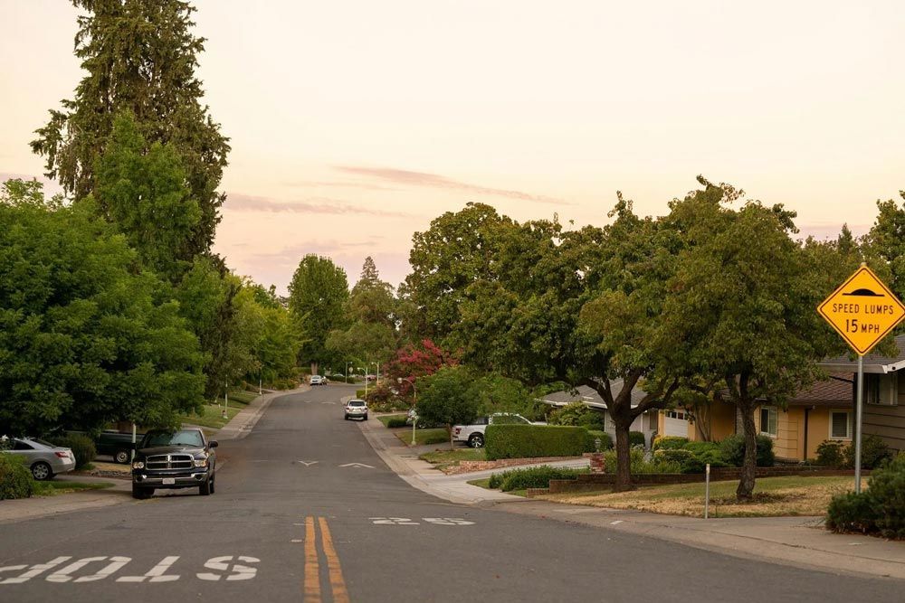 Quiet residential street in Sacramento, with single-story homes, trees, and a speed hump sign